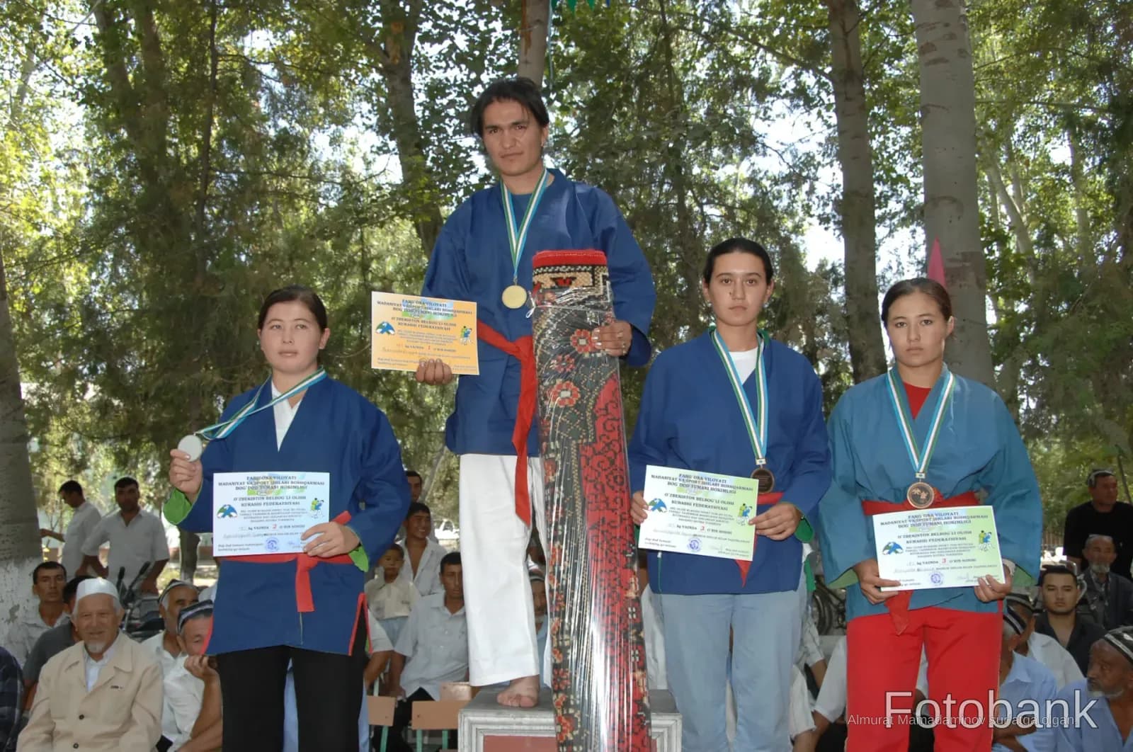 Athletes standing on a podium holding medals and certificates