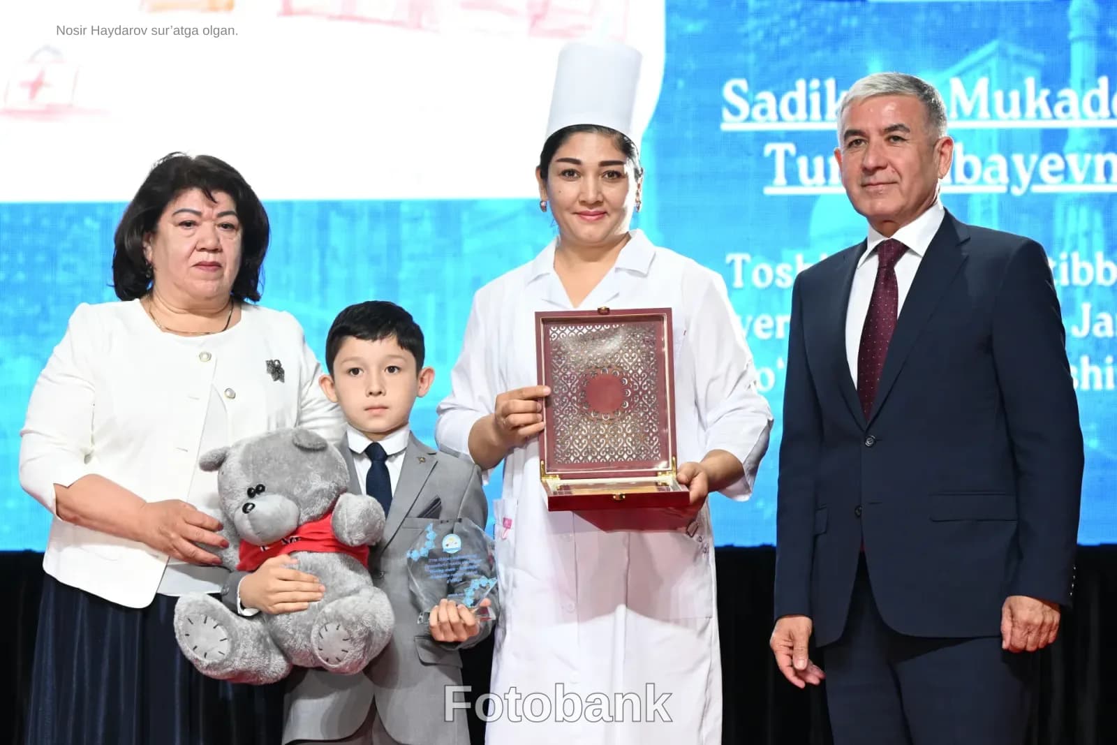 Dekorativ quti va yumshoq oʻyinchoqni ushlab turgan odamlar guruhi