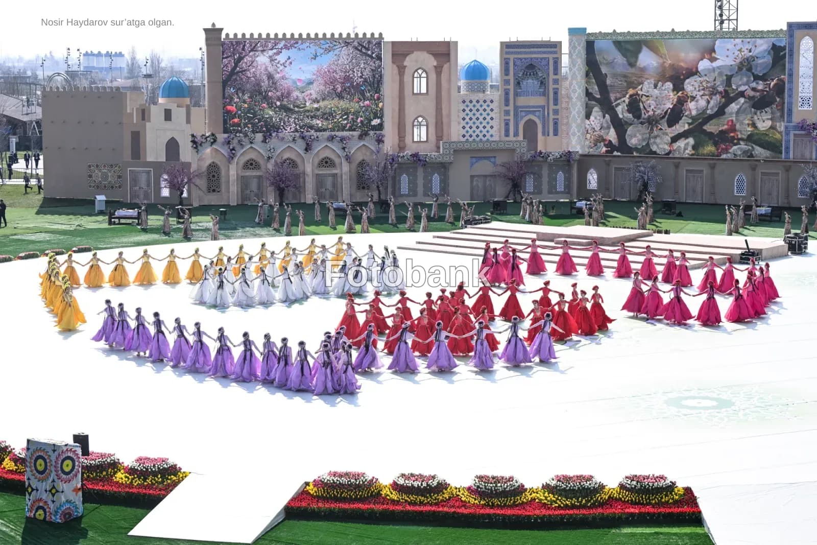 Performers in colorful dresses hold hands in formation on stage