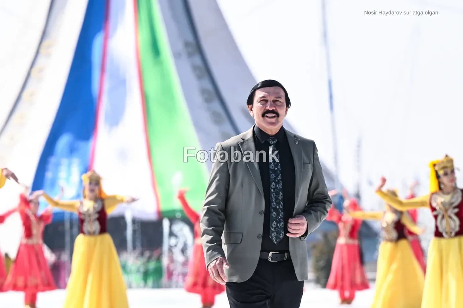 Man in suit walking outdoors with performers in the background