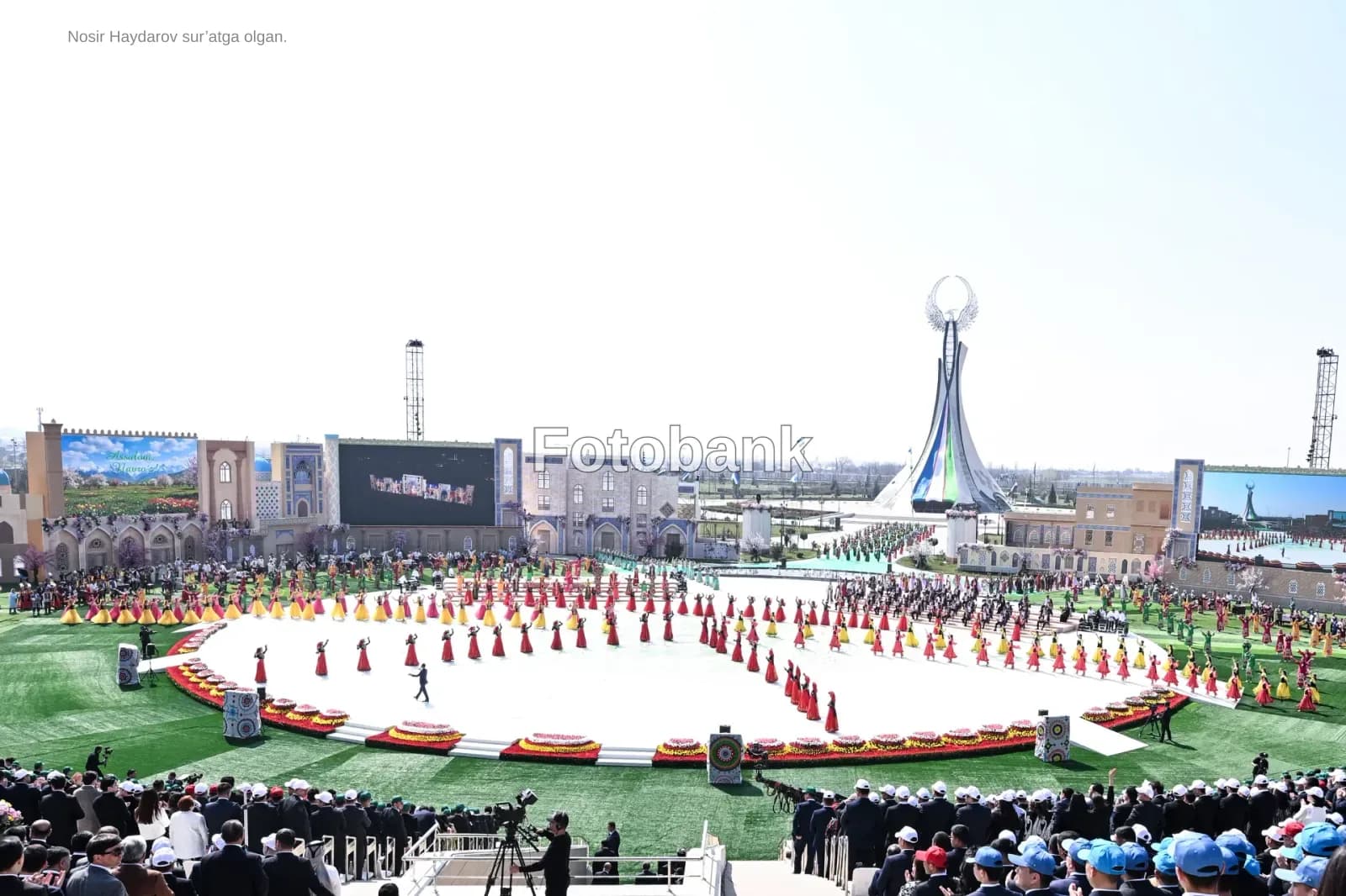 Performers in colorful dresses gather on a large outdoor stage during a public event