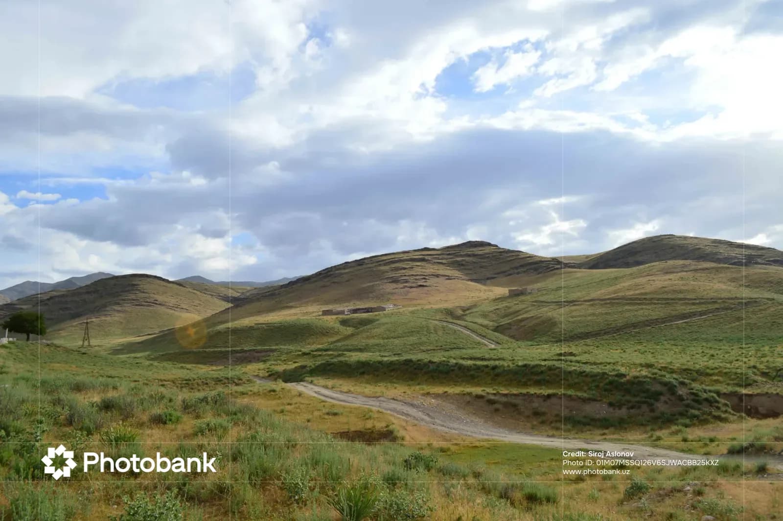 Hilly landscape with dirt roads and sparse vegetation under a cloudy sky