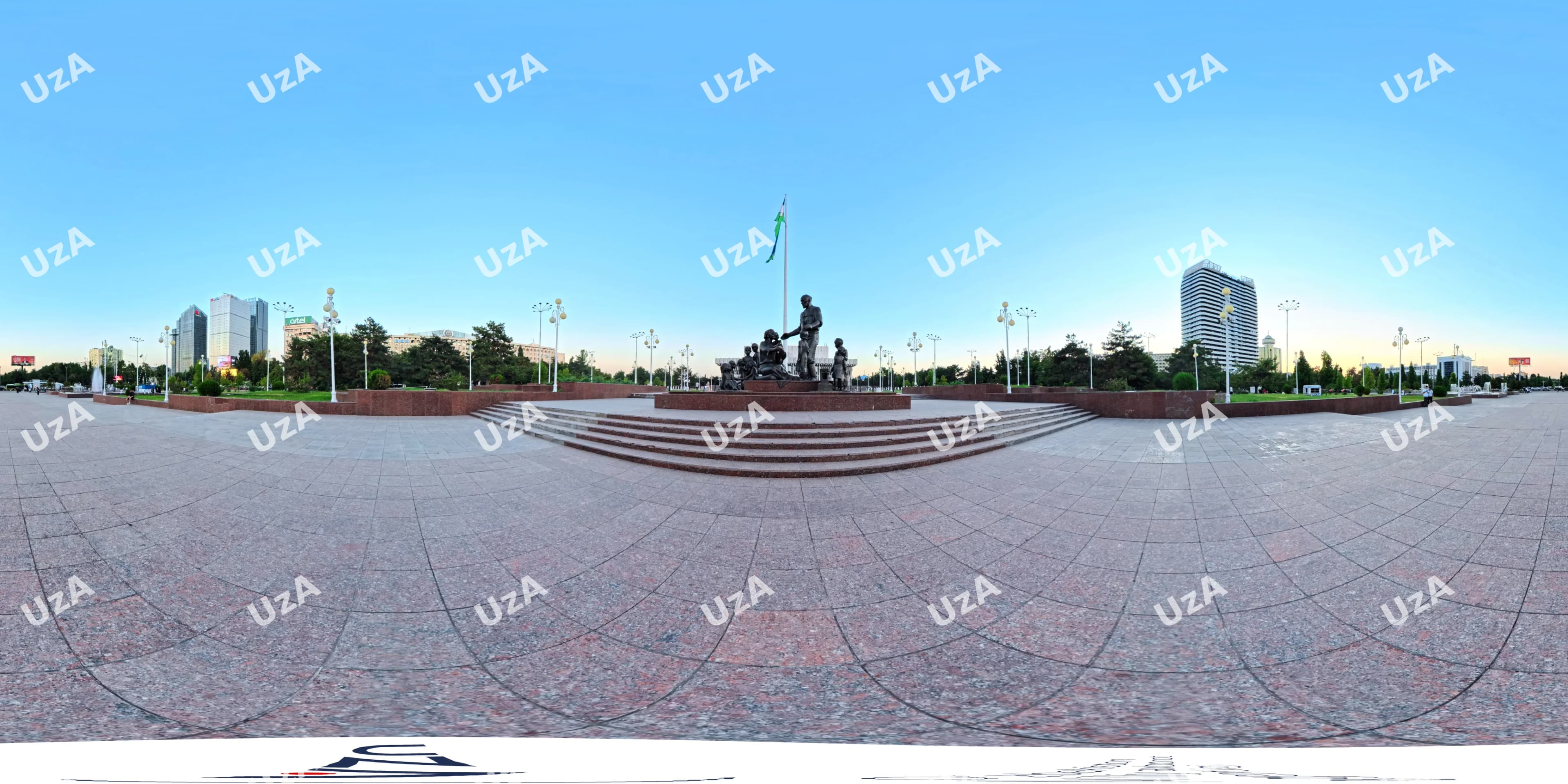 Panoramic view of a public square with a central monument and flagpole