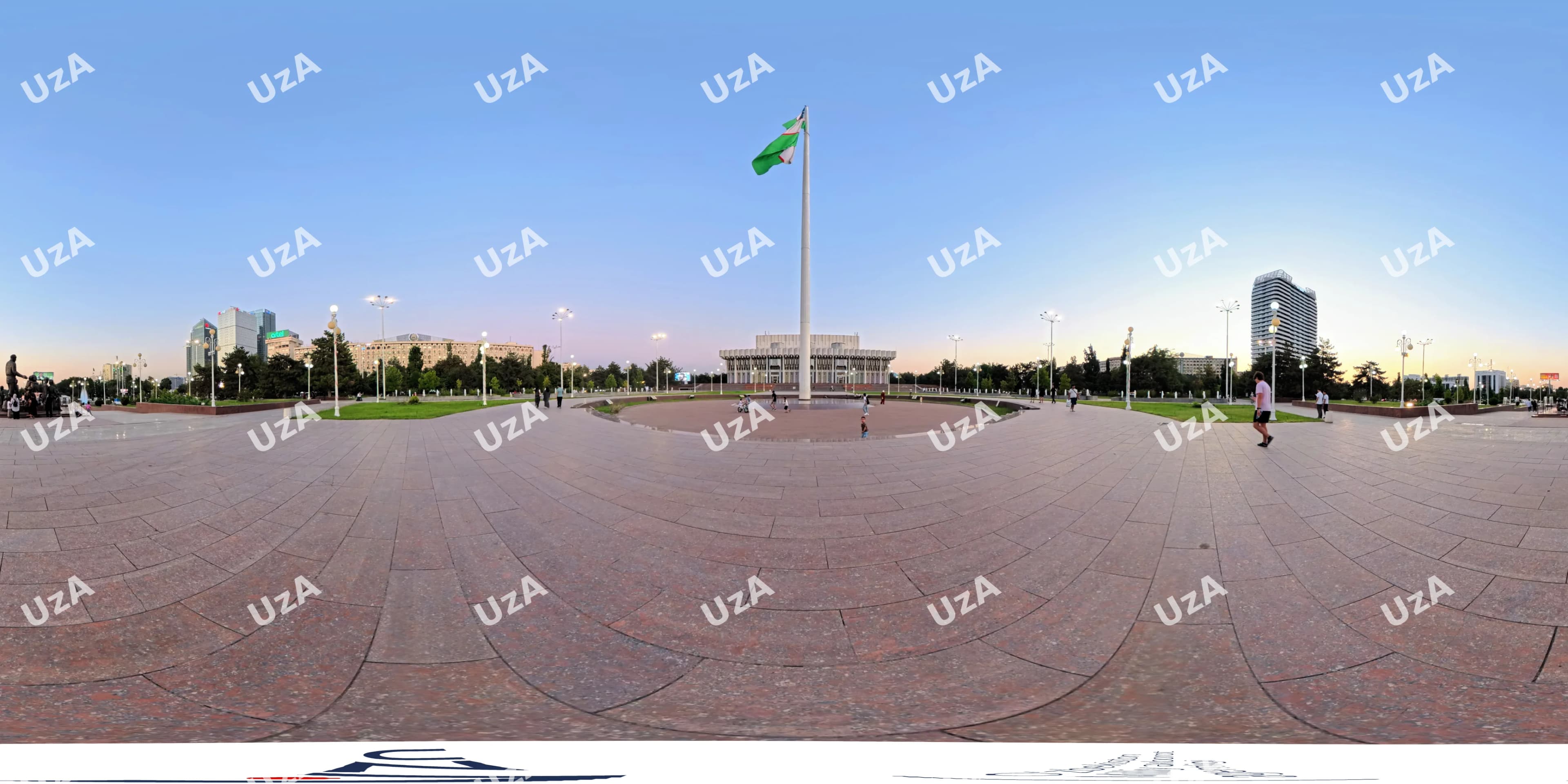Panoramic view of a large public square with a flag pole and buildings