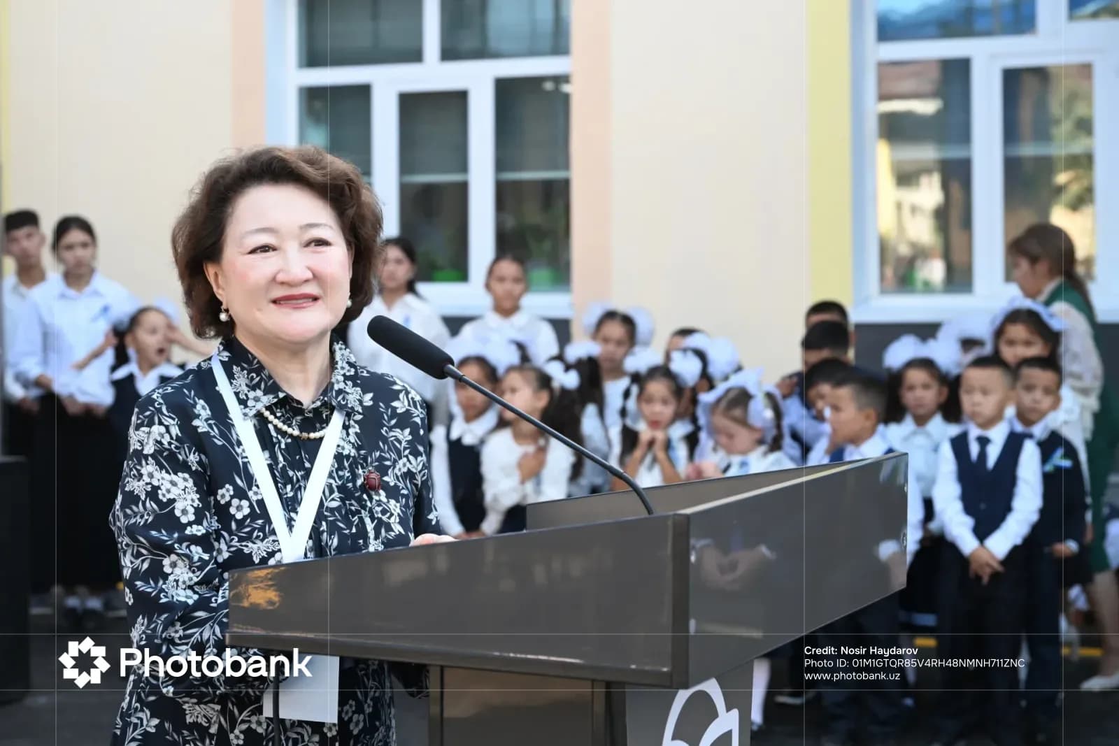 Woman speaking at a podium outdoors with people in the background