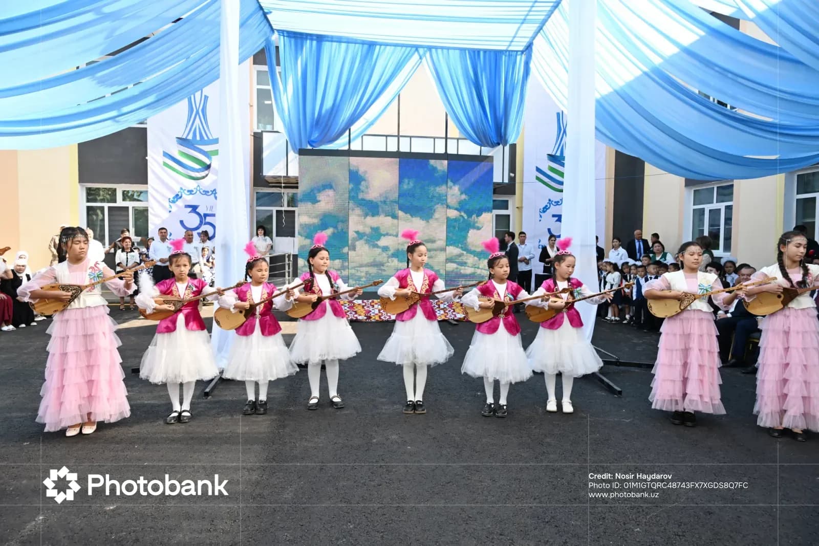 Children in traditional clothing performing with string instruments under a canopy