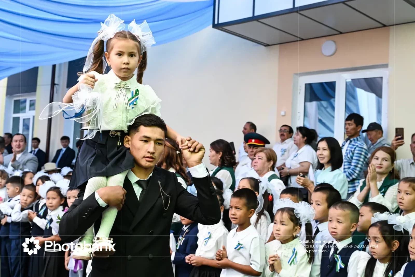 A young person carries a child on their shoulders amid a crowd