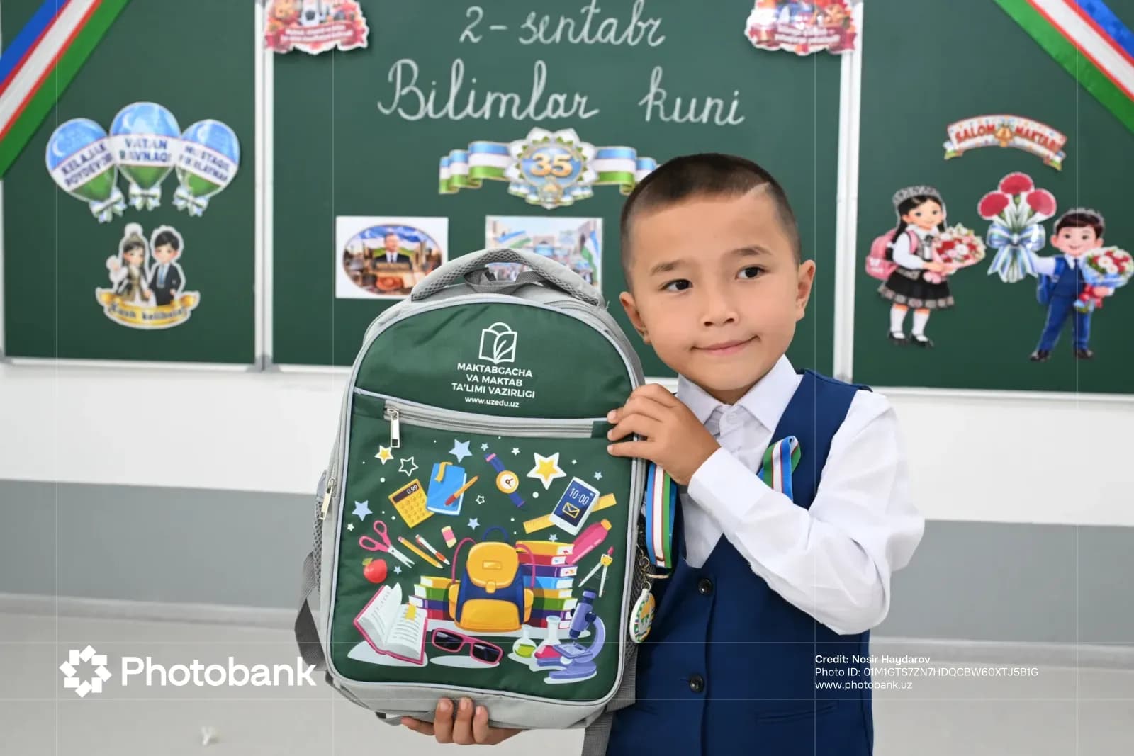 Young boy holding a school backpack in a classroom