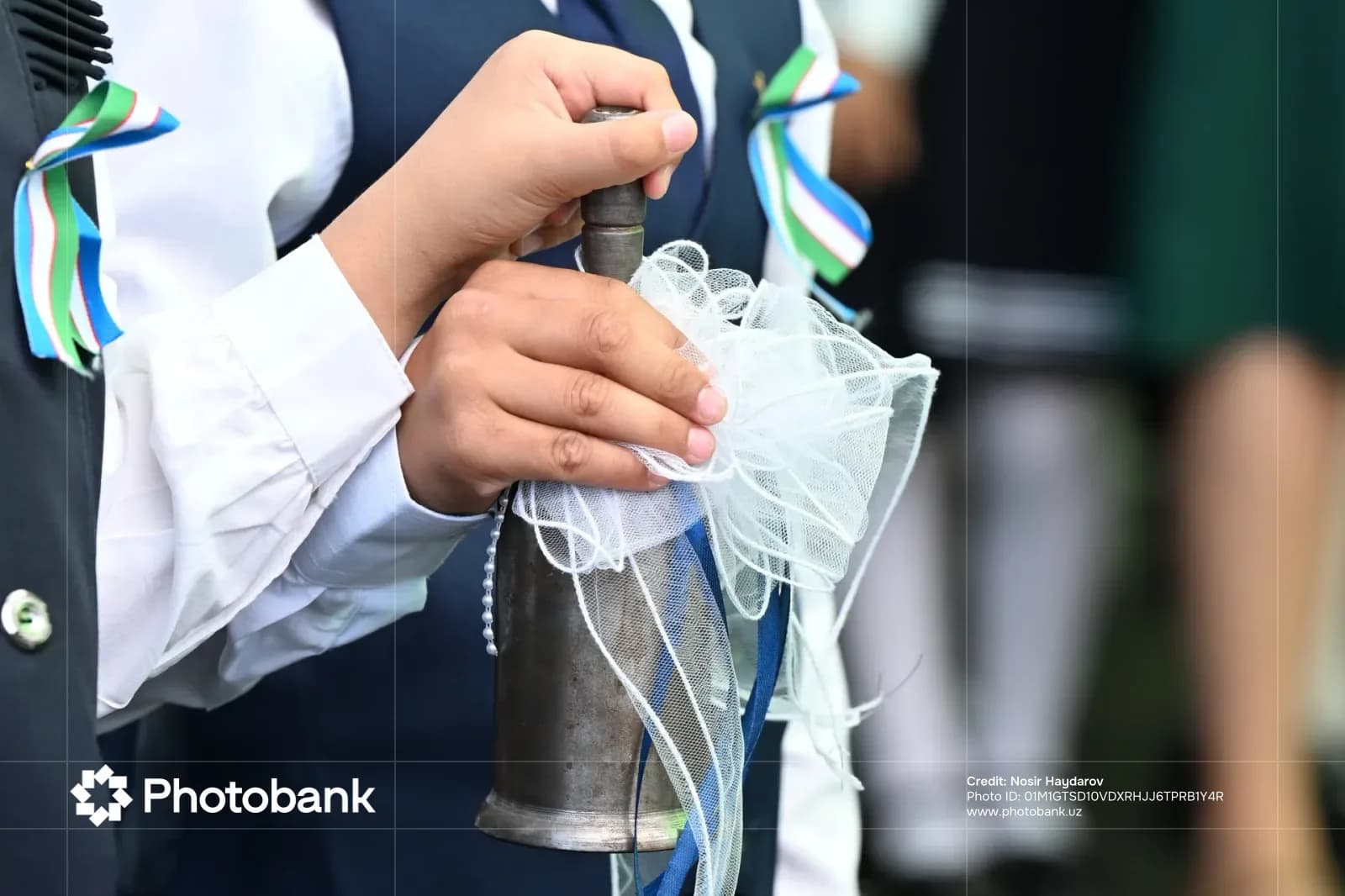 Person holding a metal bell decorated with white ribbons