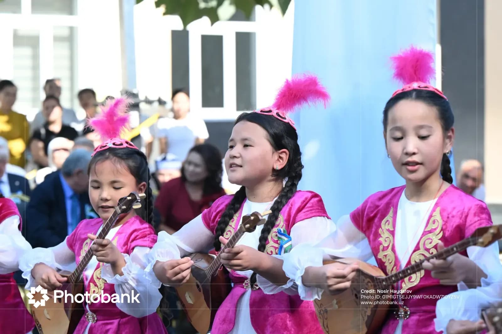 Children in traditional attire playing string instruments outdoors