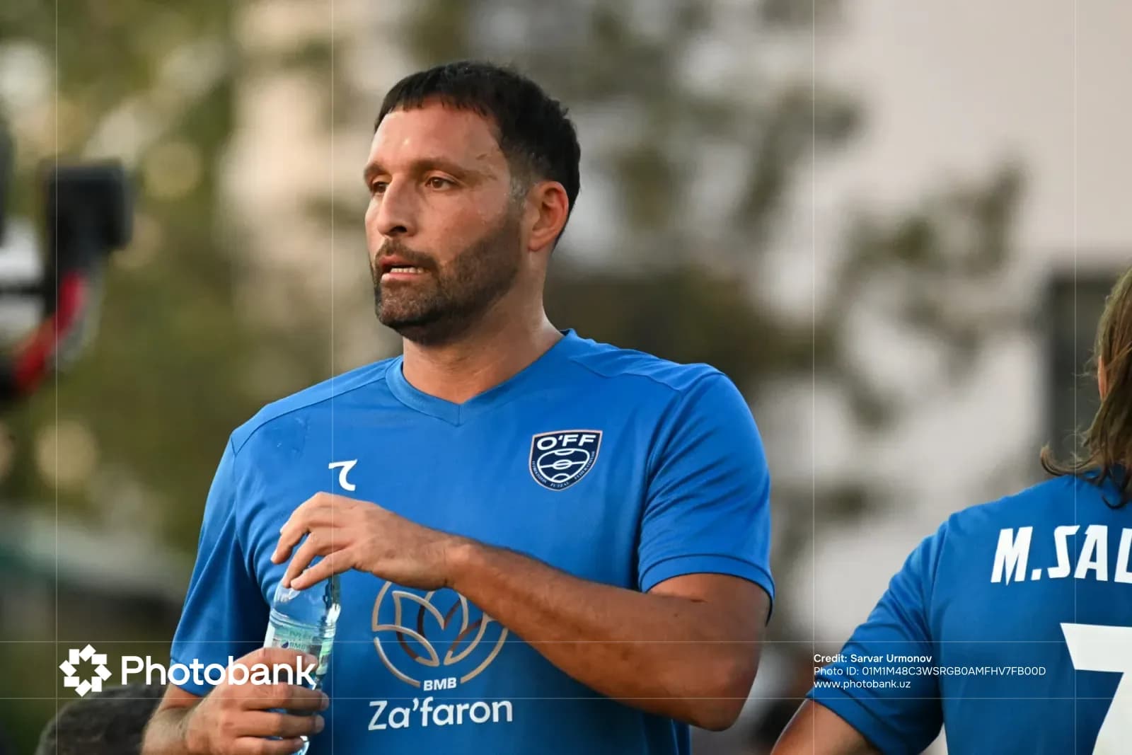 Athlete in blue sportswear holding a water bottle outdoors