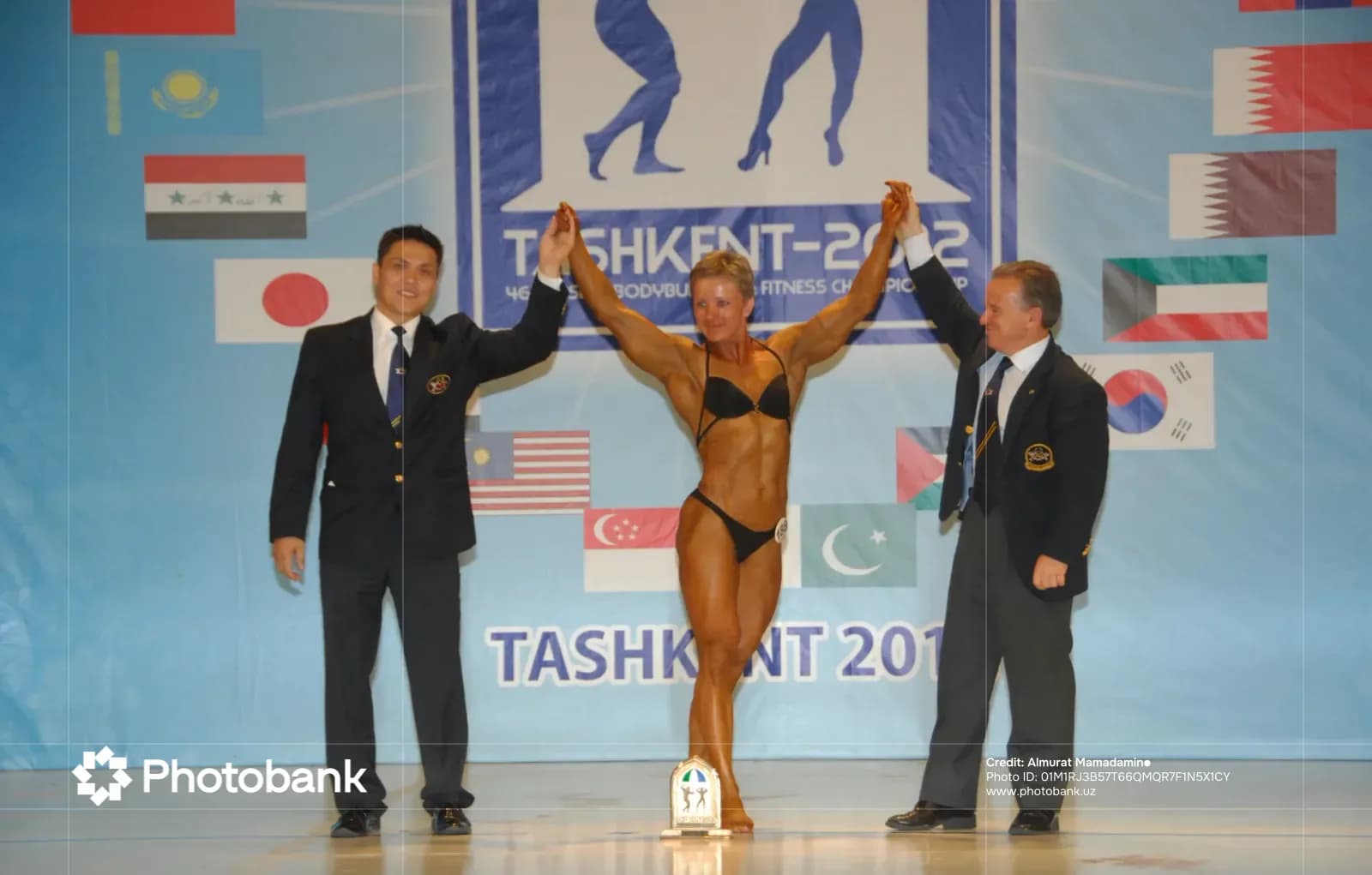 Athlete poses with officials holding hands up at a sports competition stage