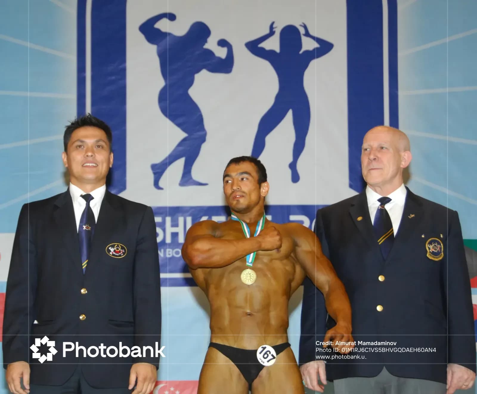 Bodybuilder wearing a medal standing with officials on stage