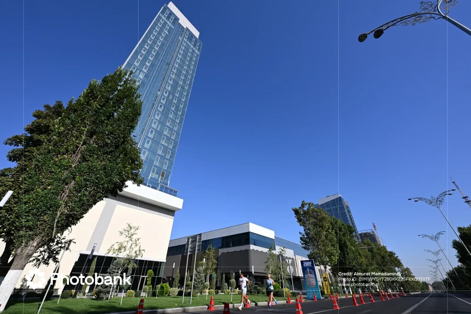 People running past modern high-rise buildings and trees on a city street