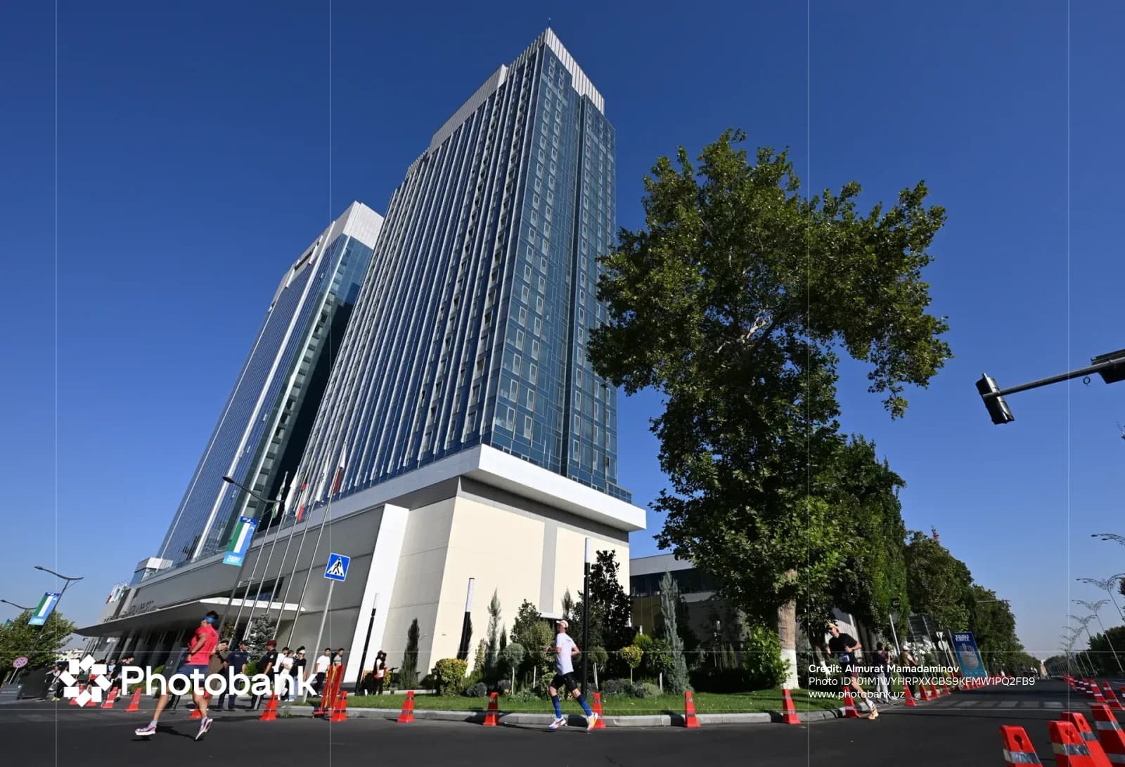 People running past modern high-rise buildings and trees on a paved street