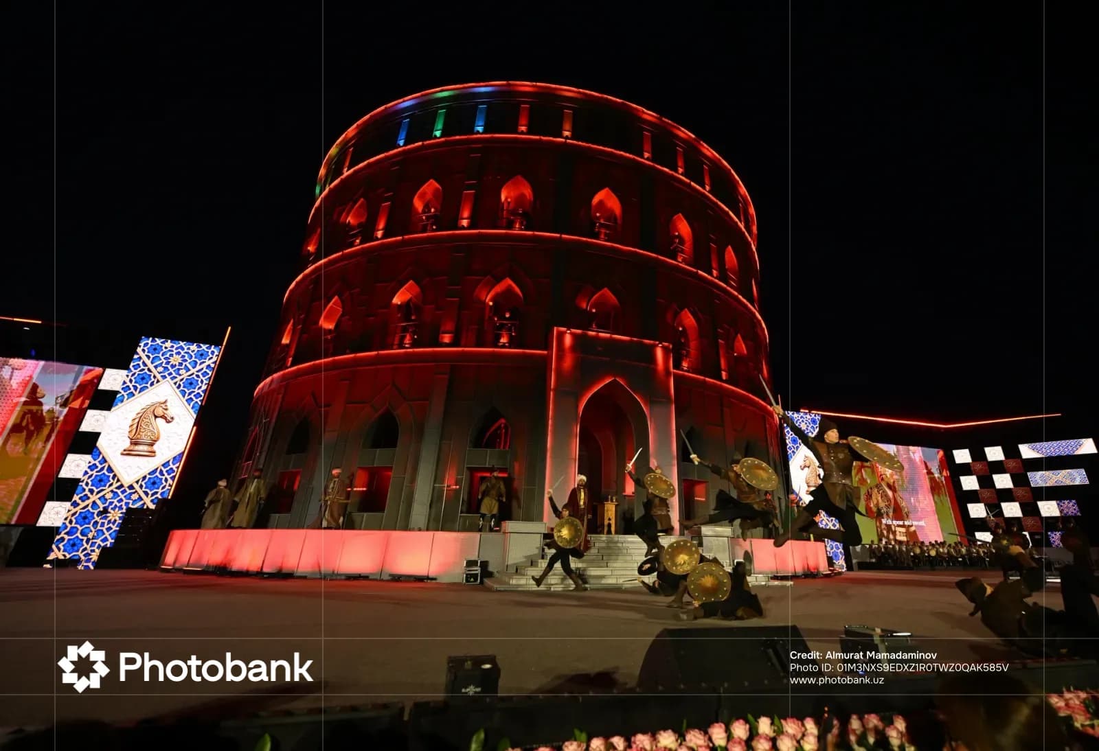 Performers in traditional attire staging a theatrical battle in front of an illuminated structure