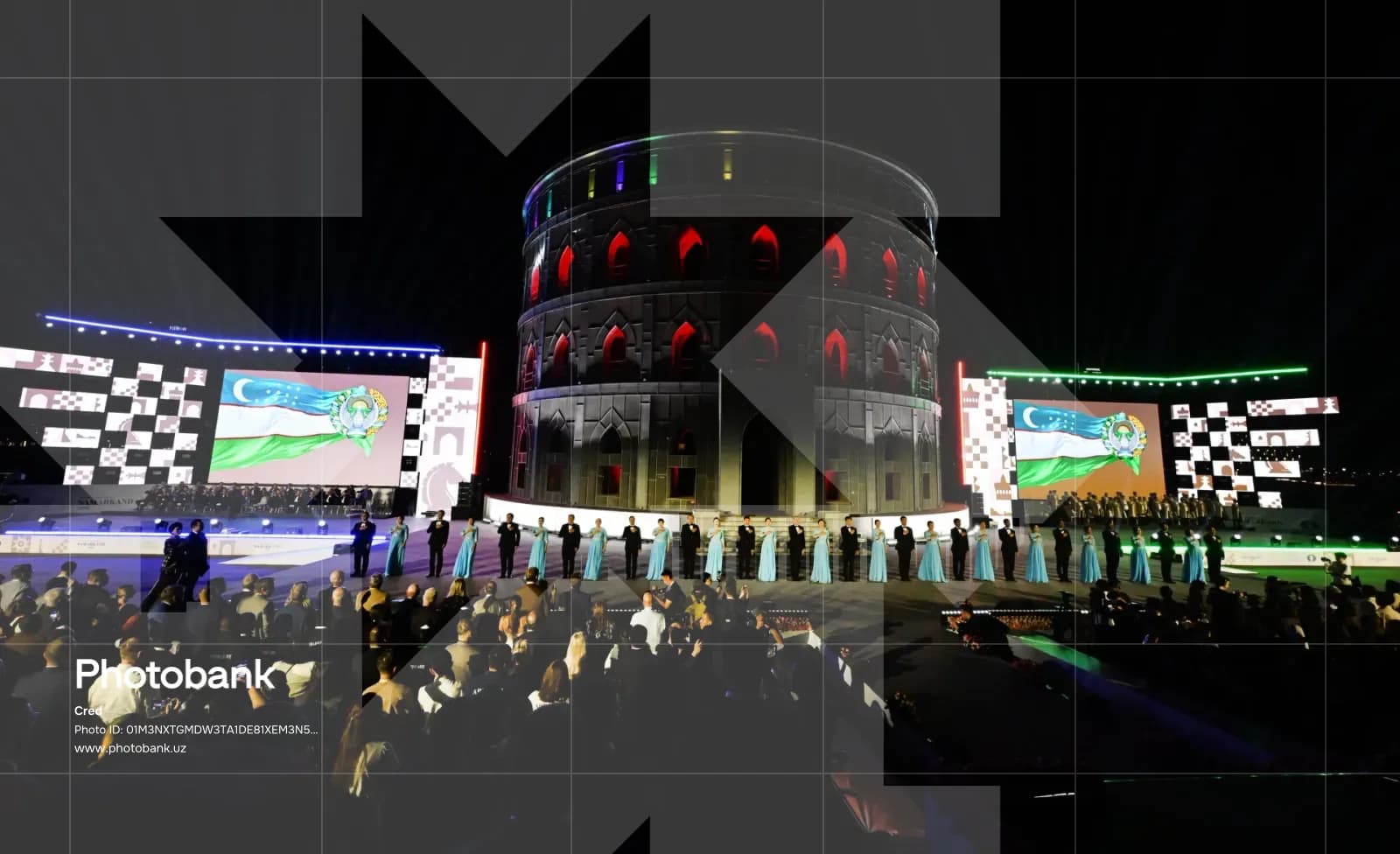 People stand on a stage before a large circular building during an evening event