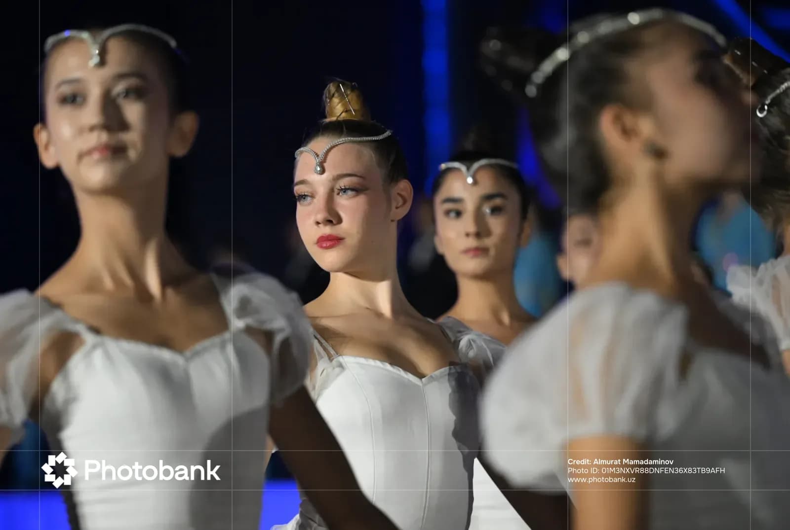 Performers in white dresses pose during a stage performance