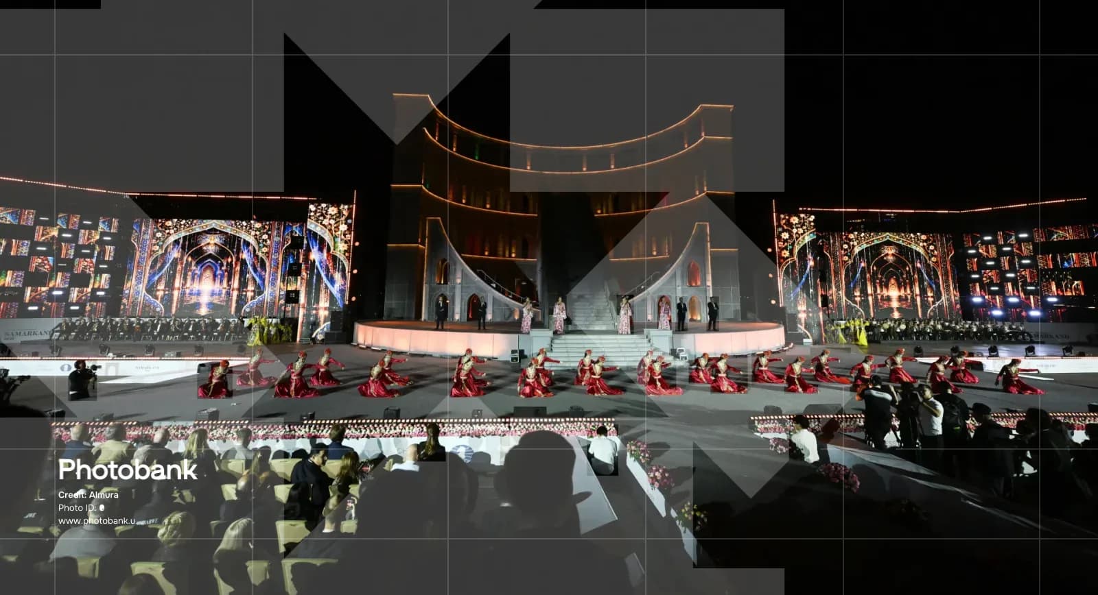 Performers in traditional clothing dance on an illuminated stage at night