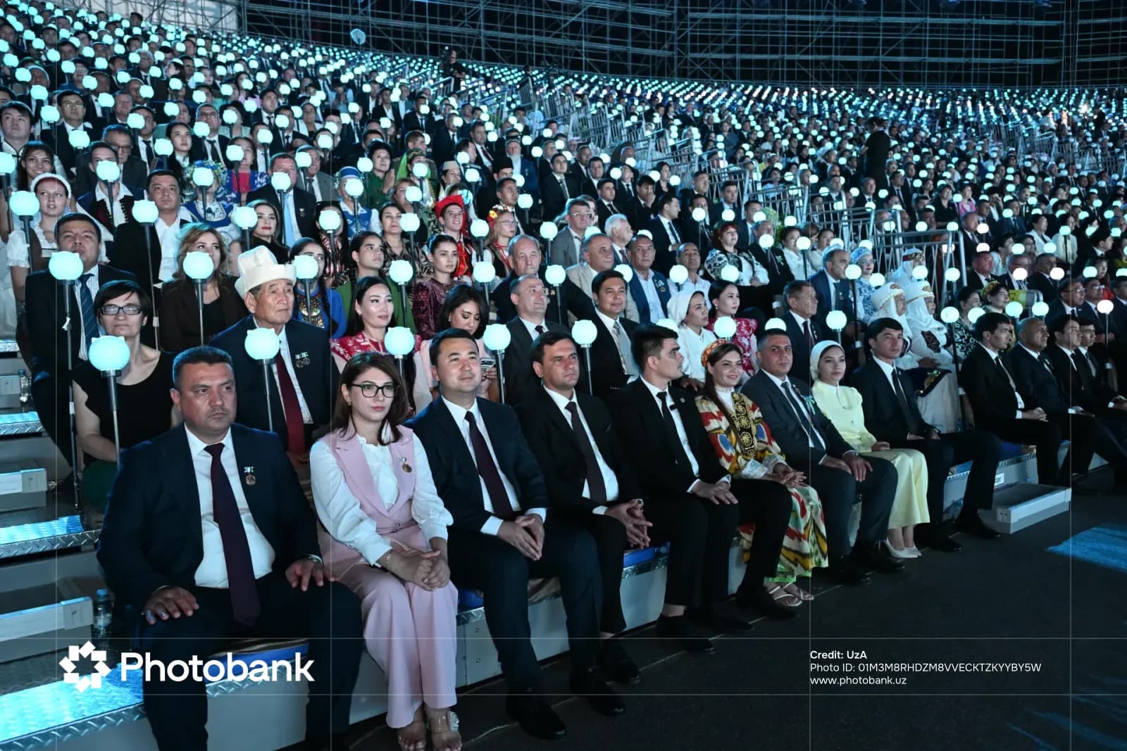 Amfiteatrda yonib turgan shar chiroqlarini ushlab oʻtirgan tomoshabinlarning katta guruhi