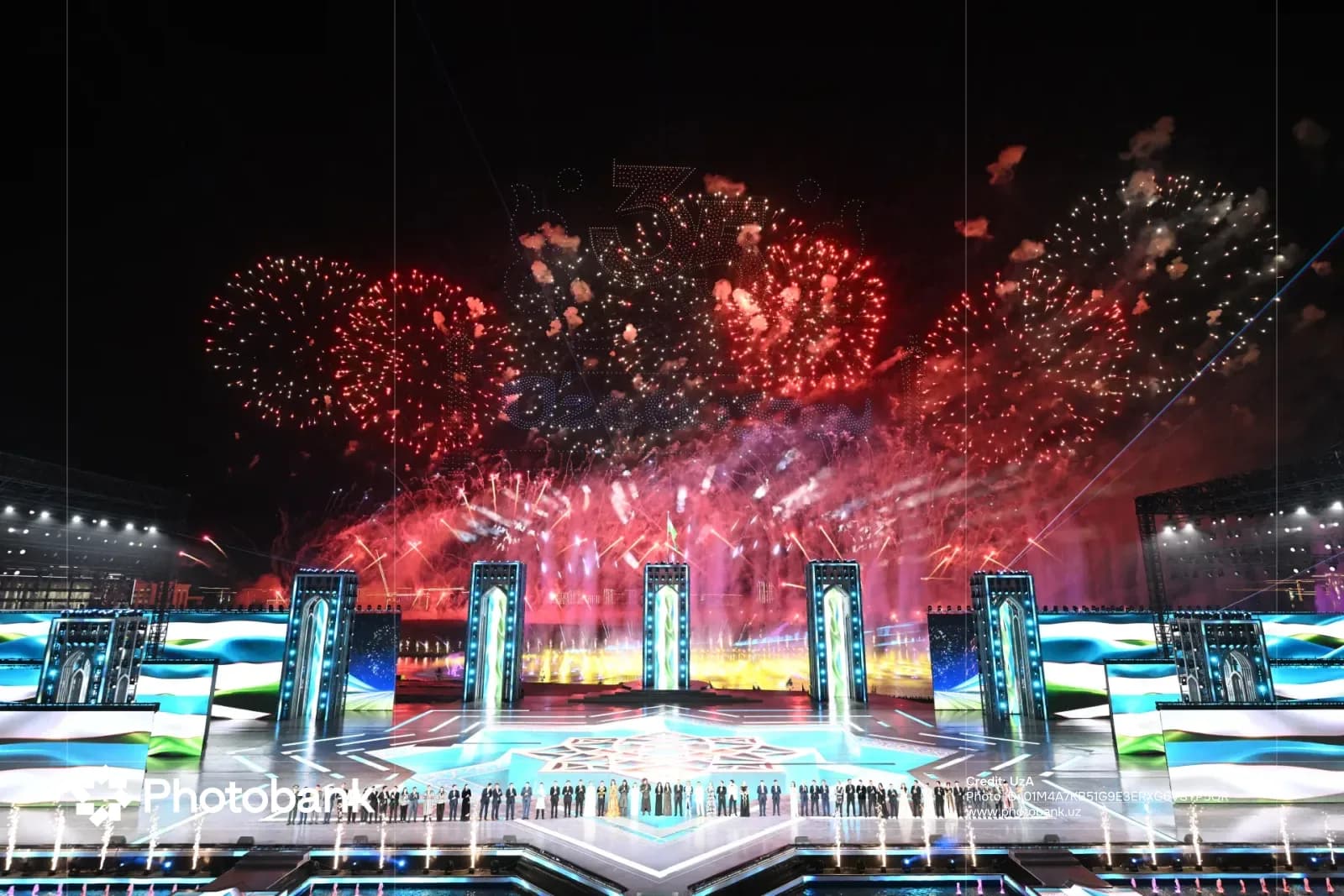 People gathered on illuminated stage during night celebration with fireworks