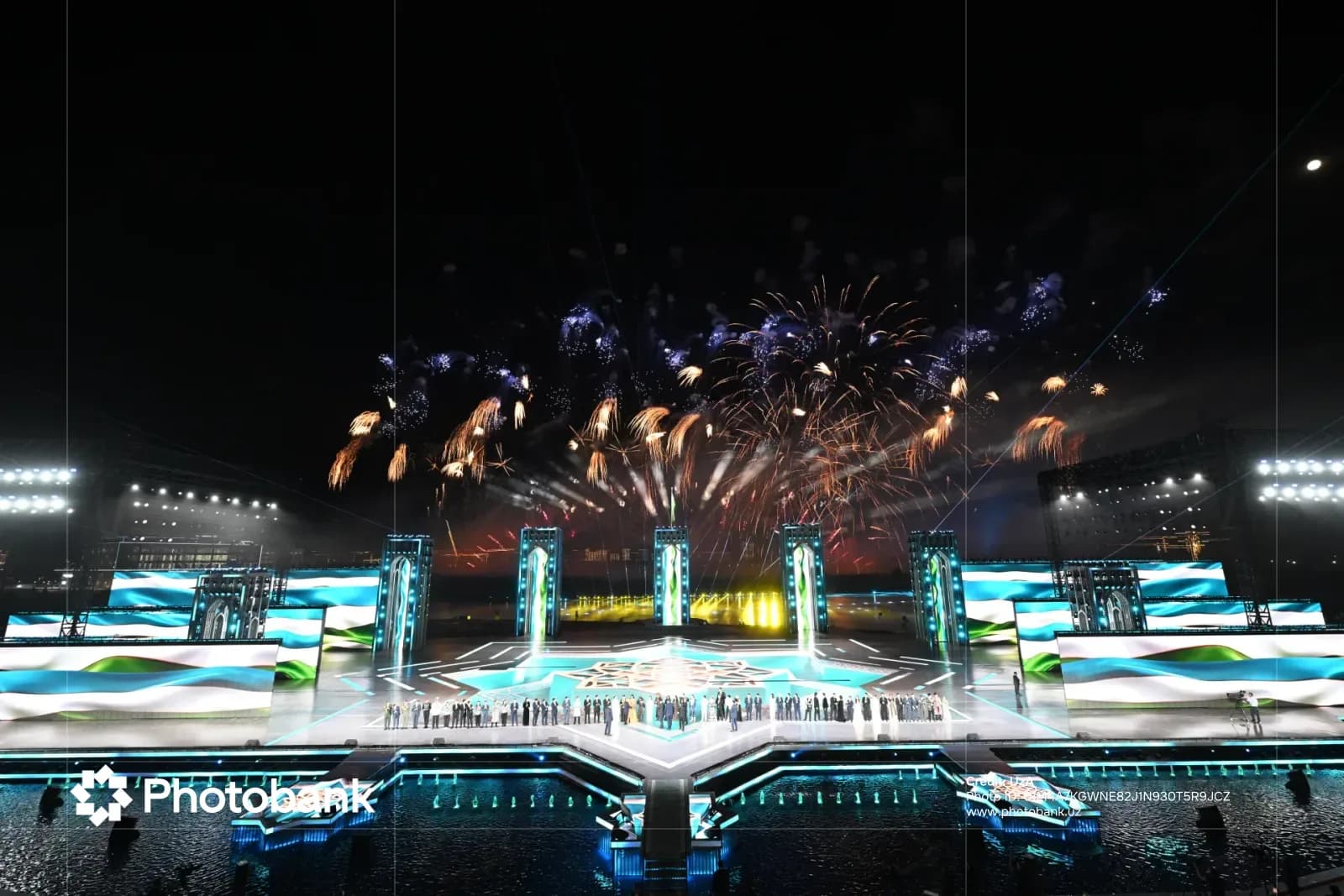 People gathered on illuminated stage during night celebration with fireworks