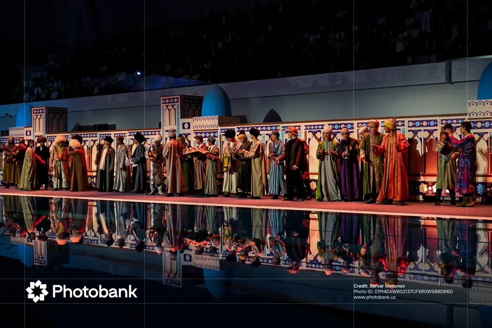 People in traditional clothing perform on a stage with reflections