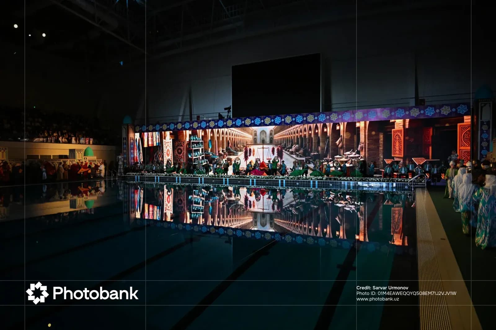 Stage performance by a large group of people in an indoor venue with a swimming pool