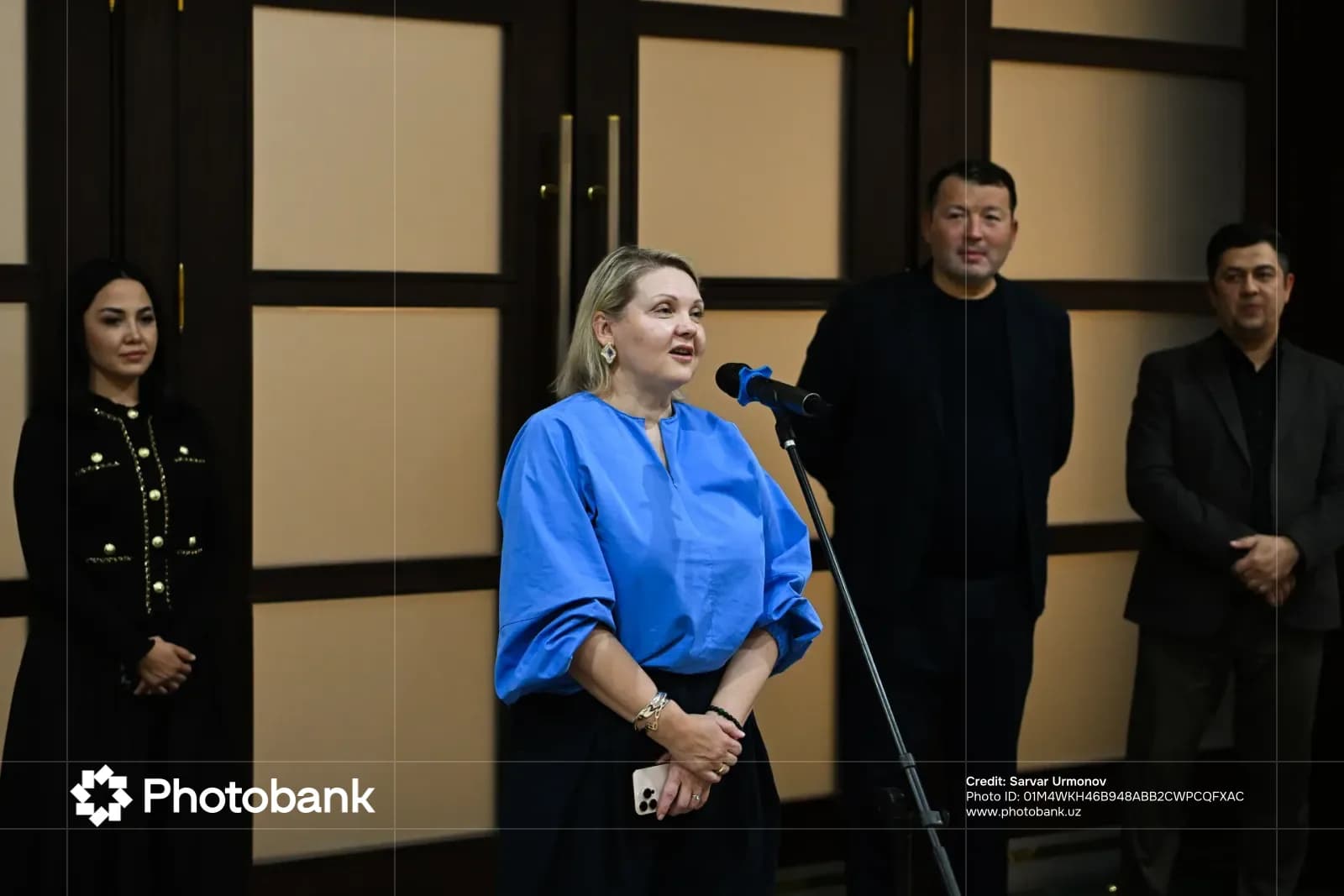 Woman speaking into microphone with people standing nearby