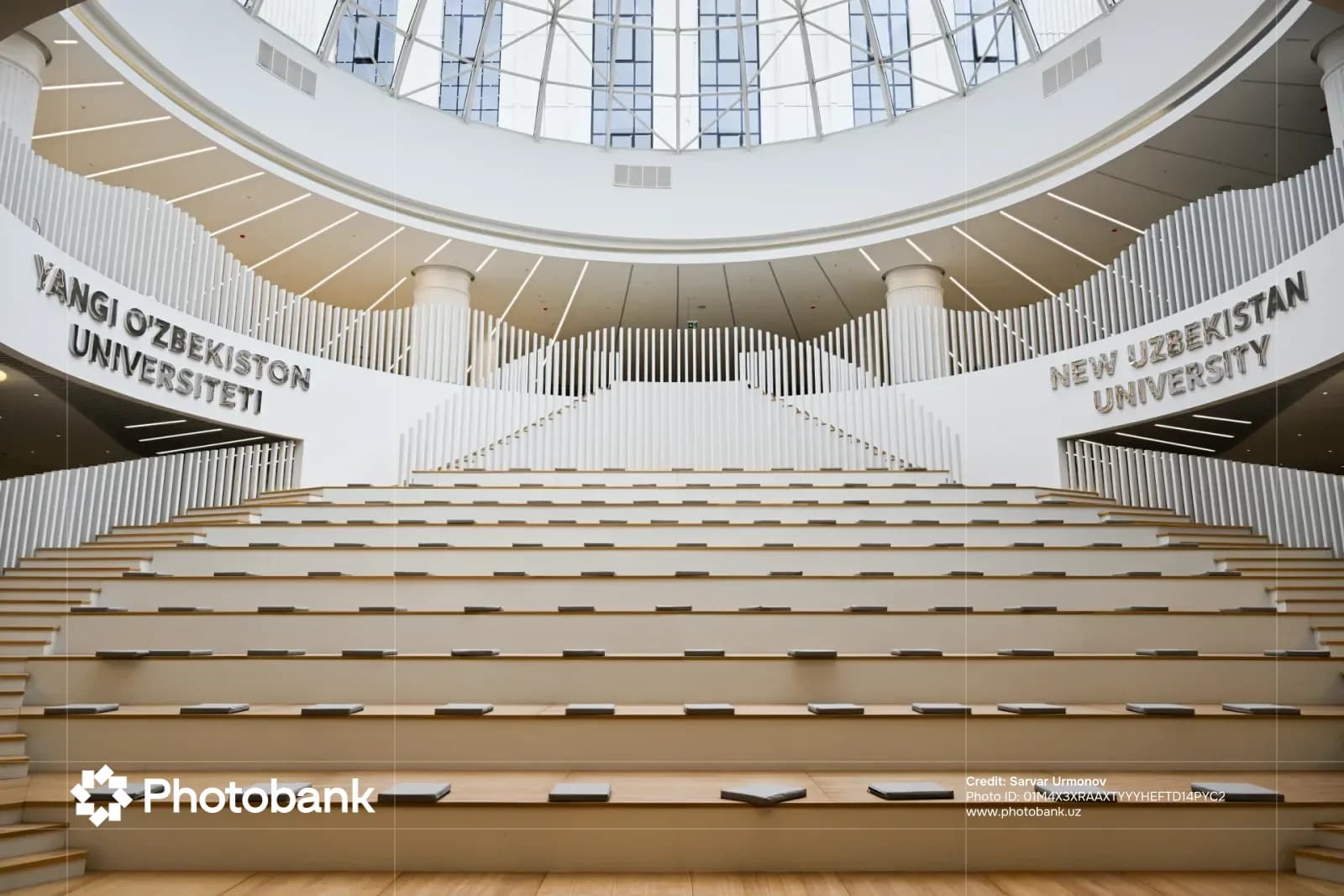 Interior view of a modern university amphitheater with tiered wooden seating under a glass dome