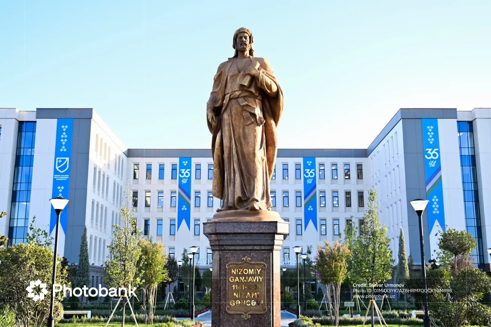 Bronze monument stands before a modern administrative building with blue vertical banners