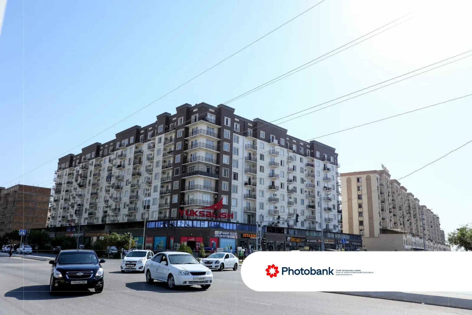 Автомобили, едущие по городской улице рядом с многоэтажными жилыми домами