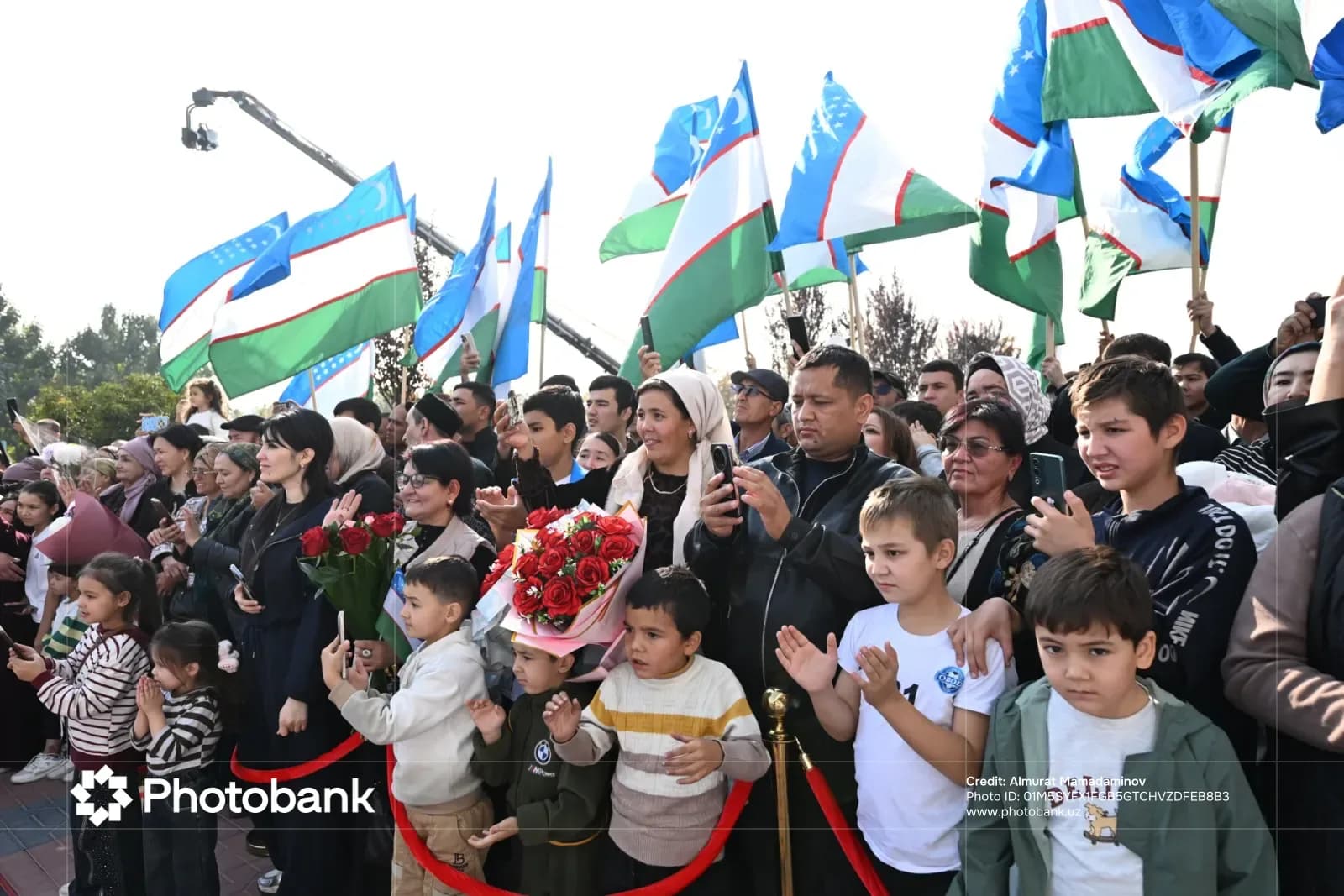 Crowd of people holding flags and flowers outdoors