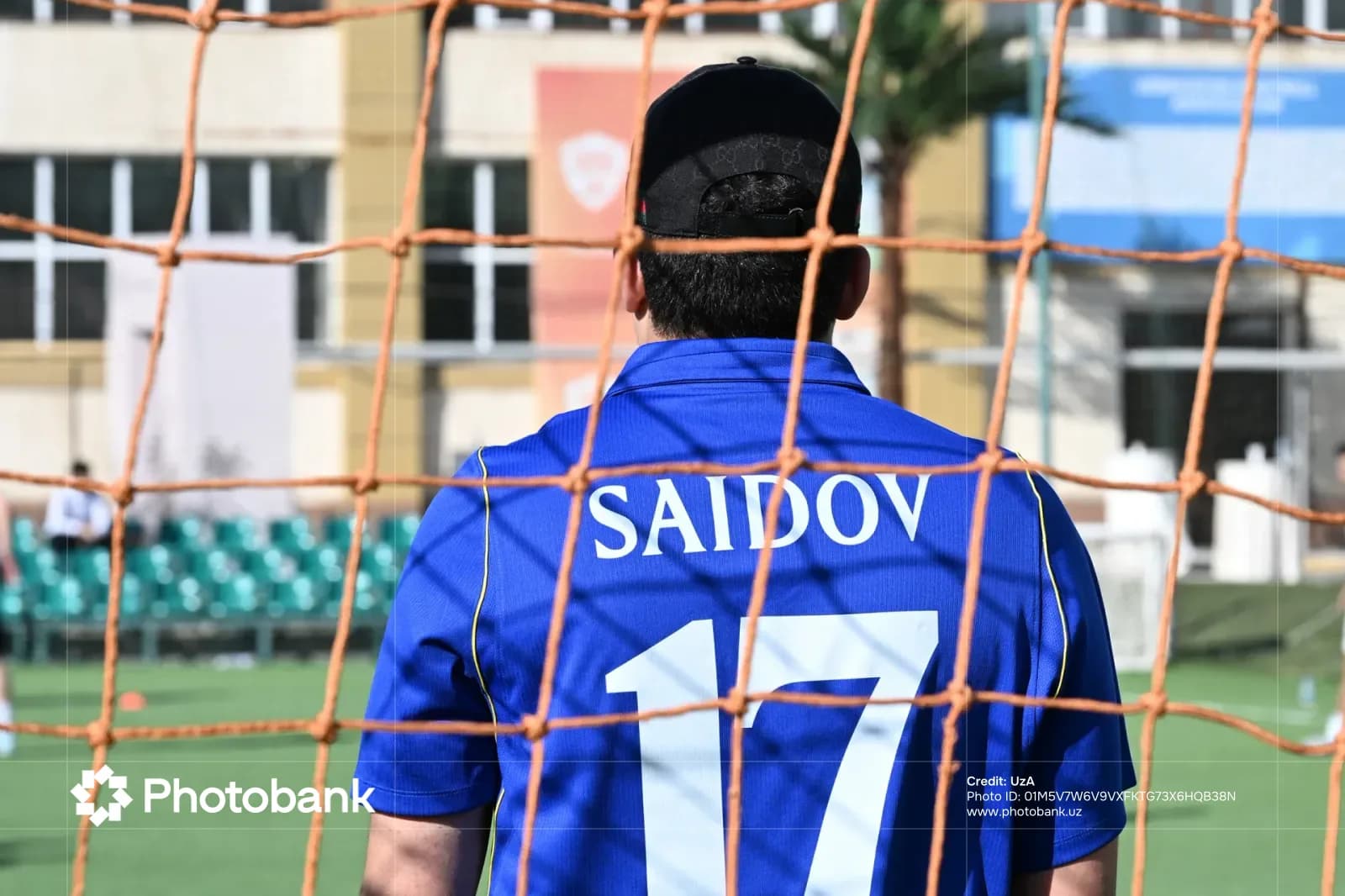 Rear view of a person wearing a blue sports jersey standing near a net on a field