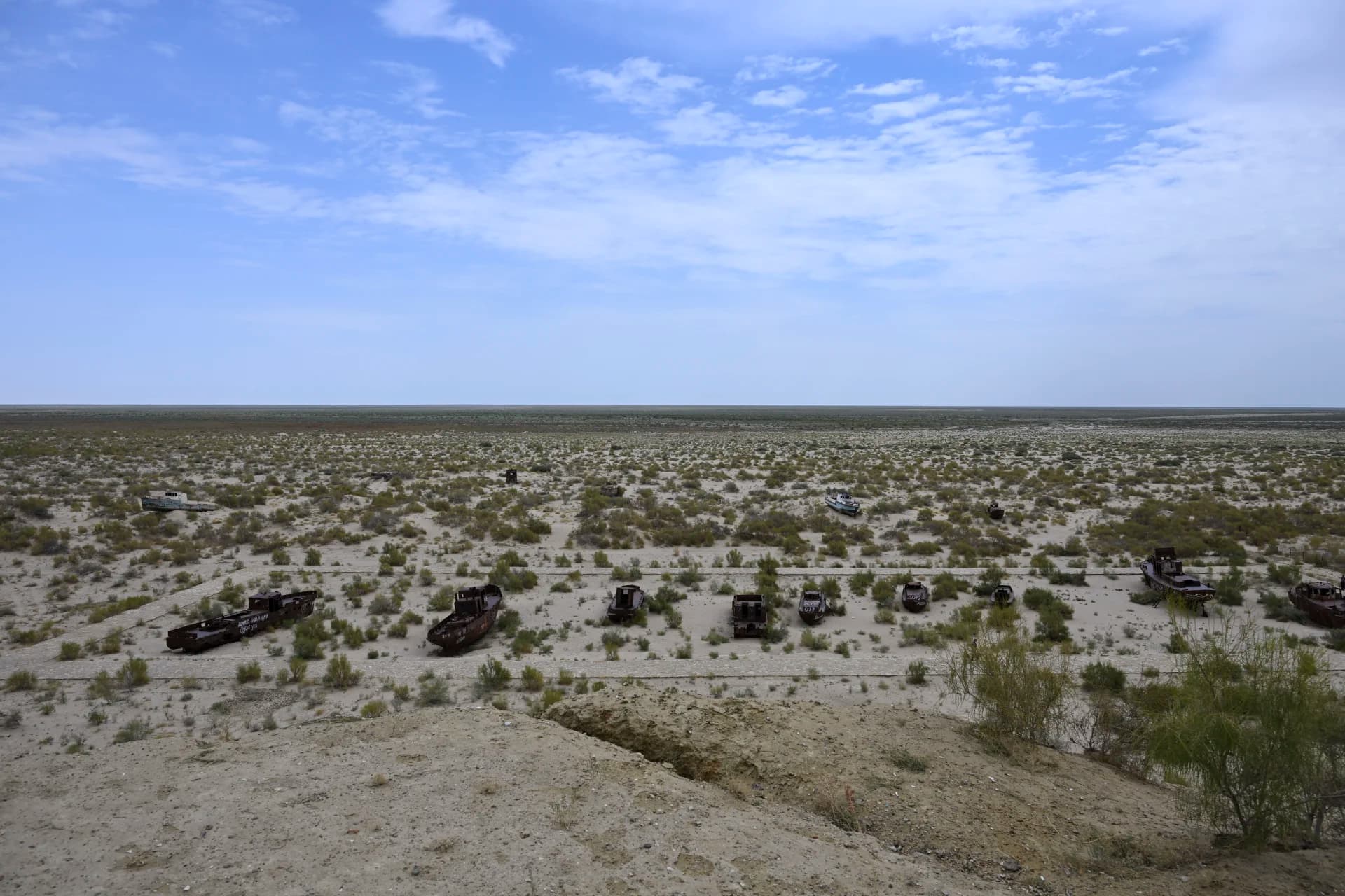 Rusted ships resting on a dry desert landscape under a cloudy sky