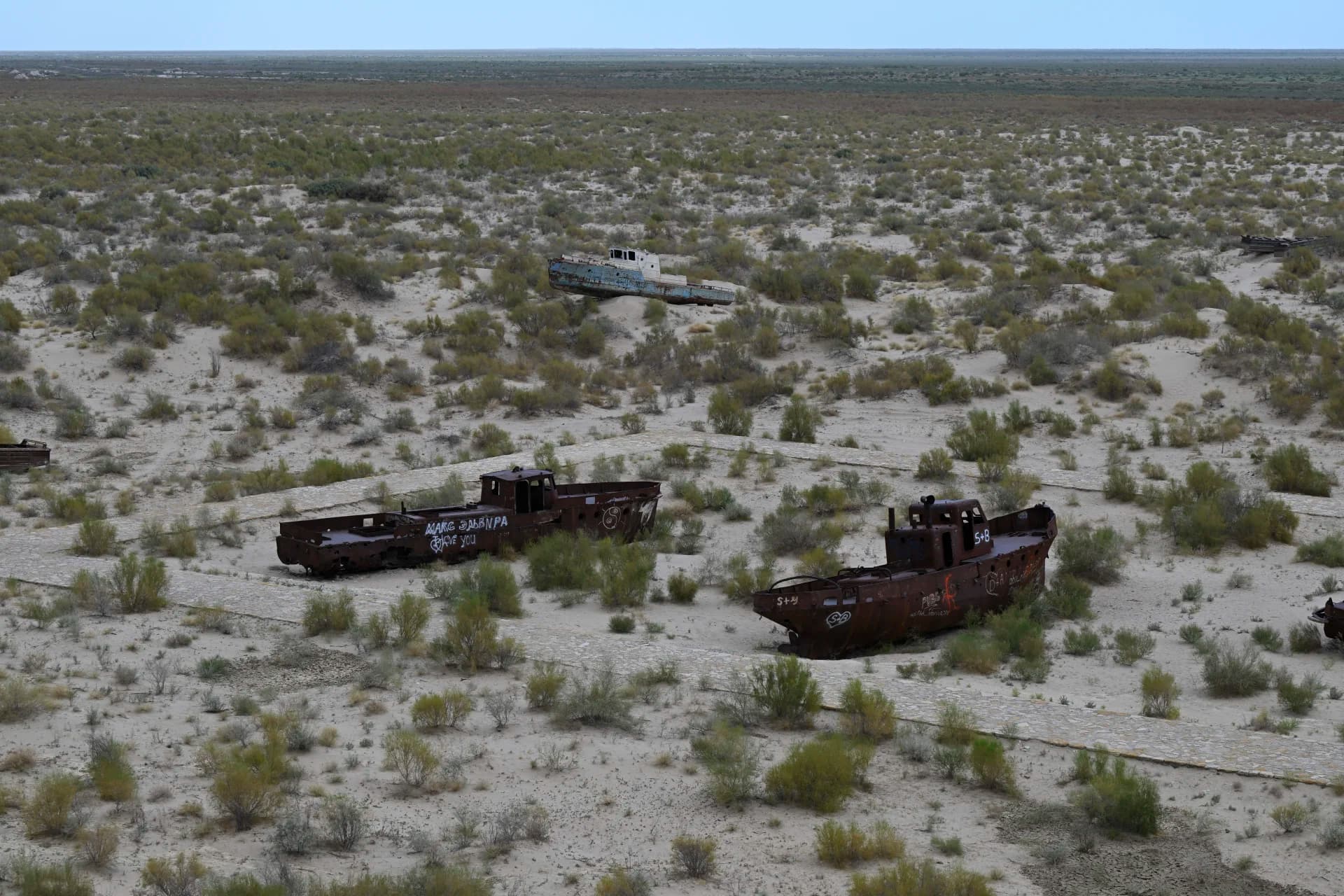 Abandoned rusty ships resting in a dry landscape with sparse vegetation