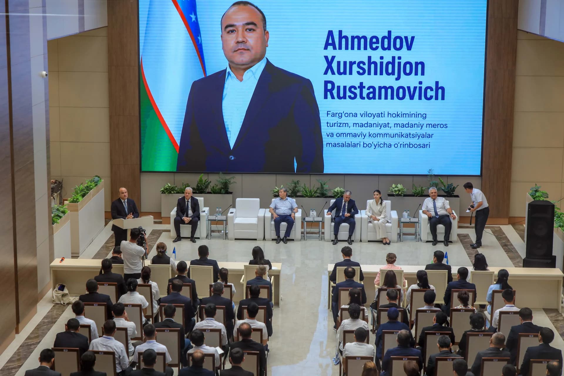 Люди, посещающие конференцию в закрытом зале с большим цифровым экраном, отображающим текст