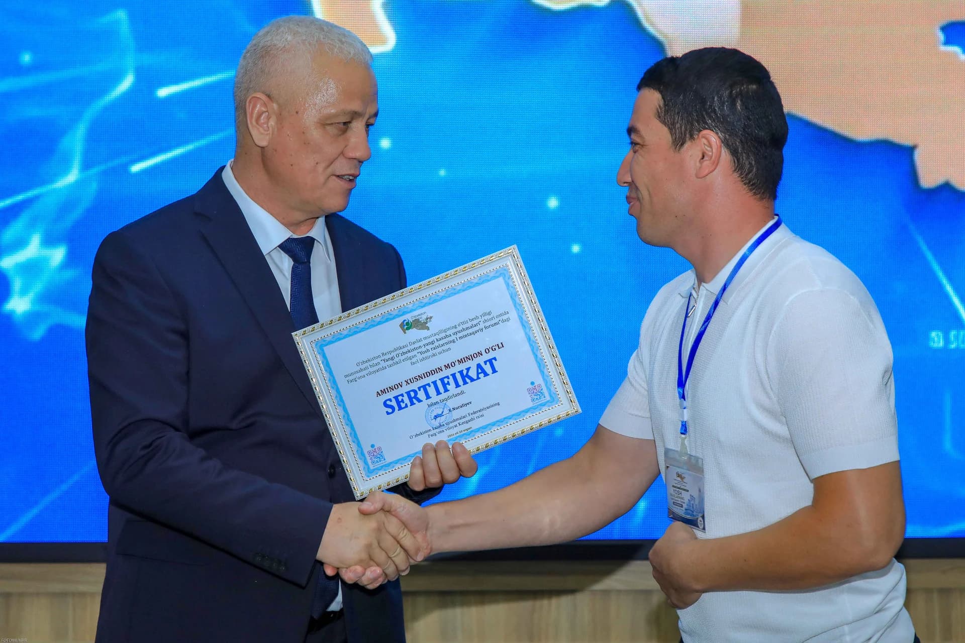 Двое мужчин пожимают друг другу руки, держа сертификат