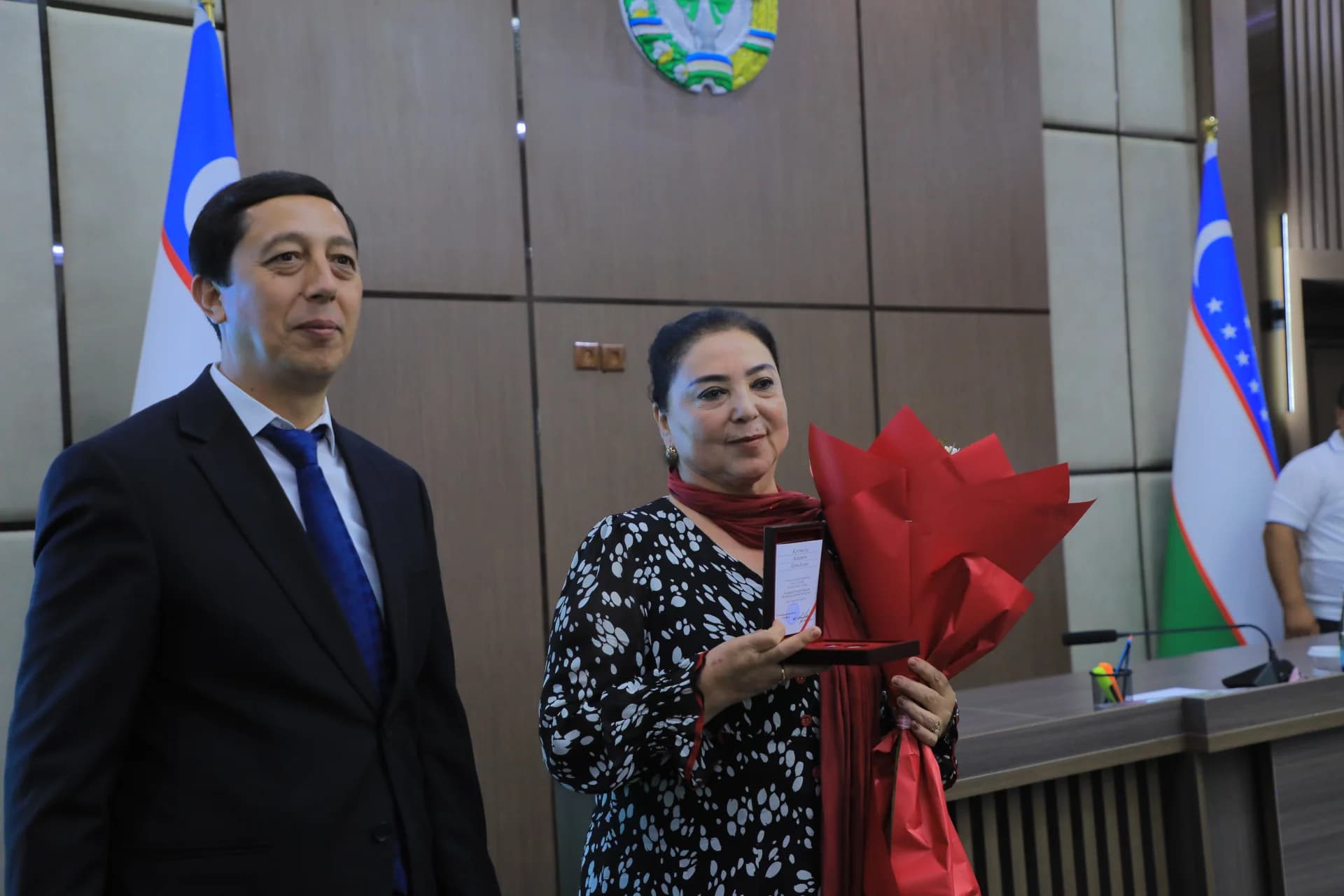 People posing with flowers and award inside a room with flags