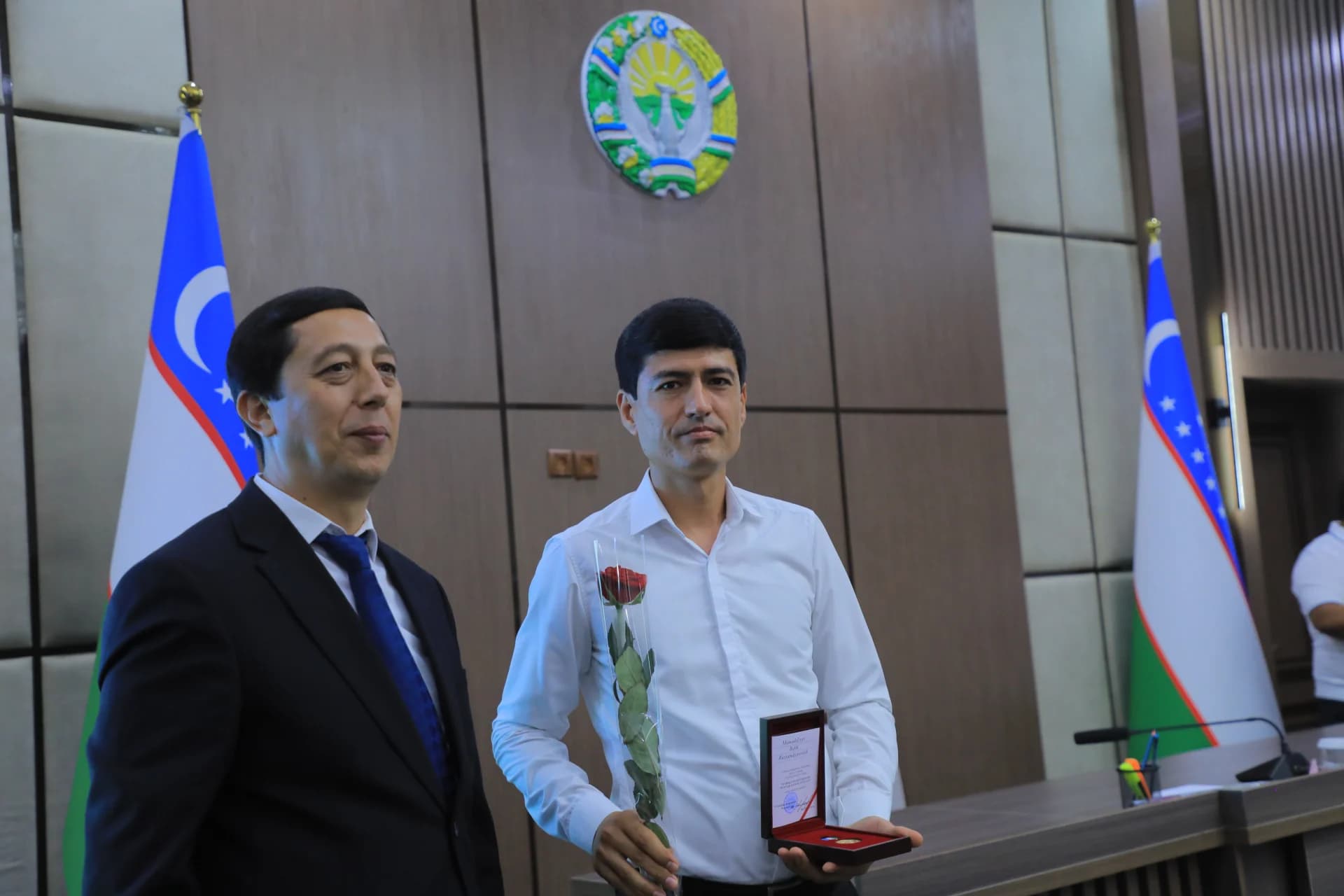 Two men standing together indoors with flags and an emblem