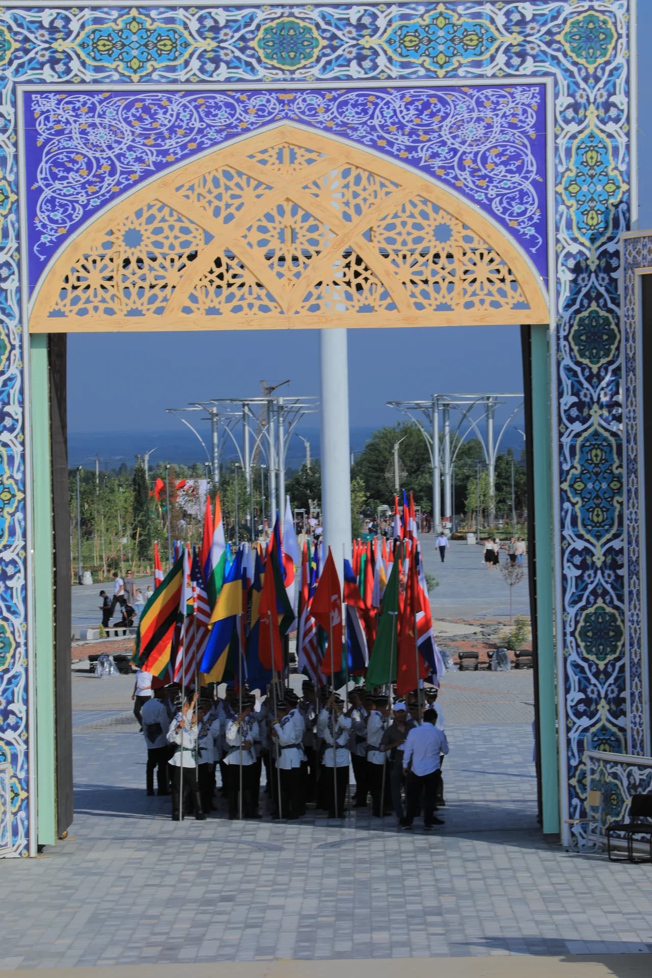 People carrying multiple national flags under an ornate arched gateway