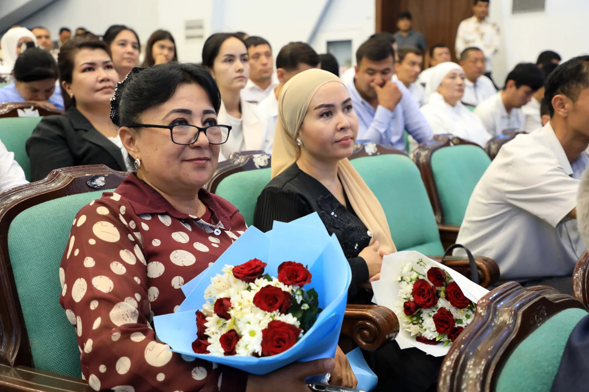 People sitting in an audience holding flower bouquets