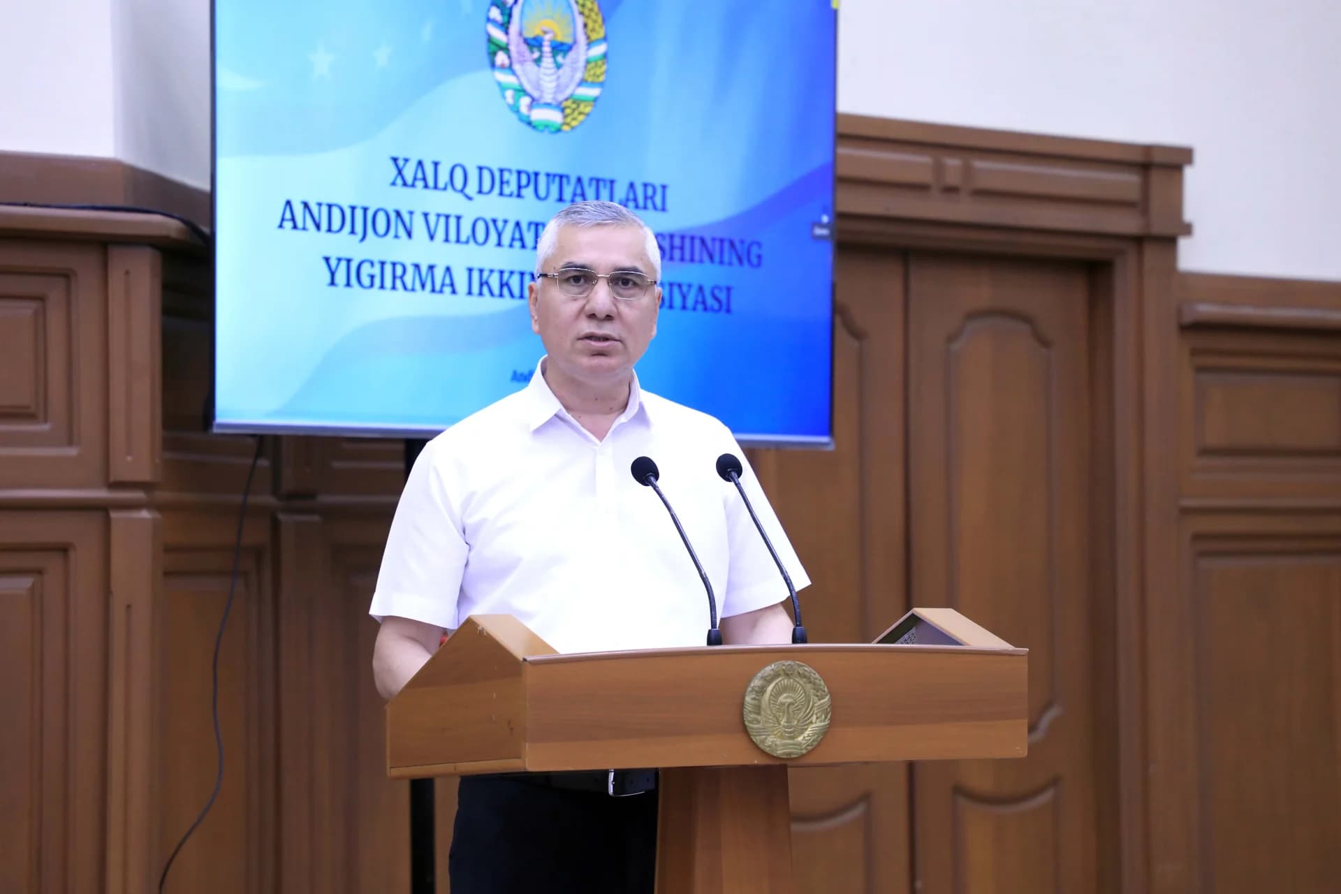 Man speaking at a wooden podium in an indoor meeting