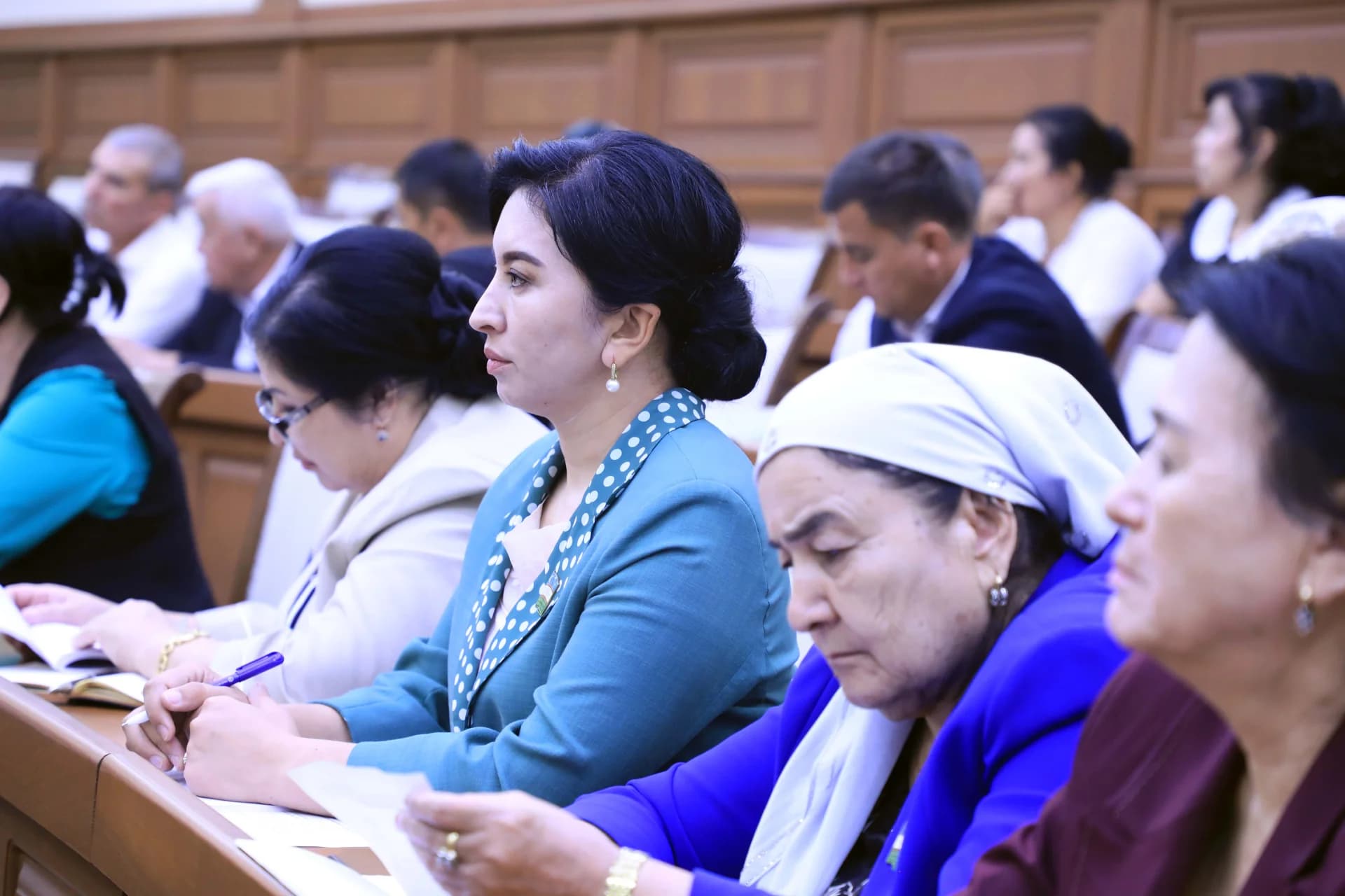People attending a conference seated at wooden desks