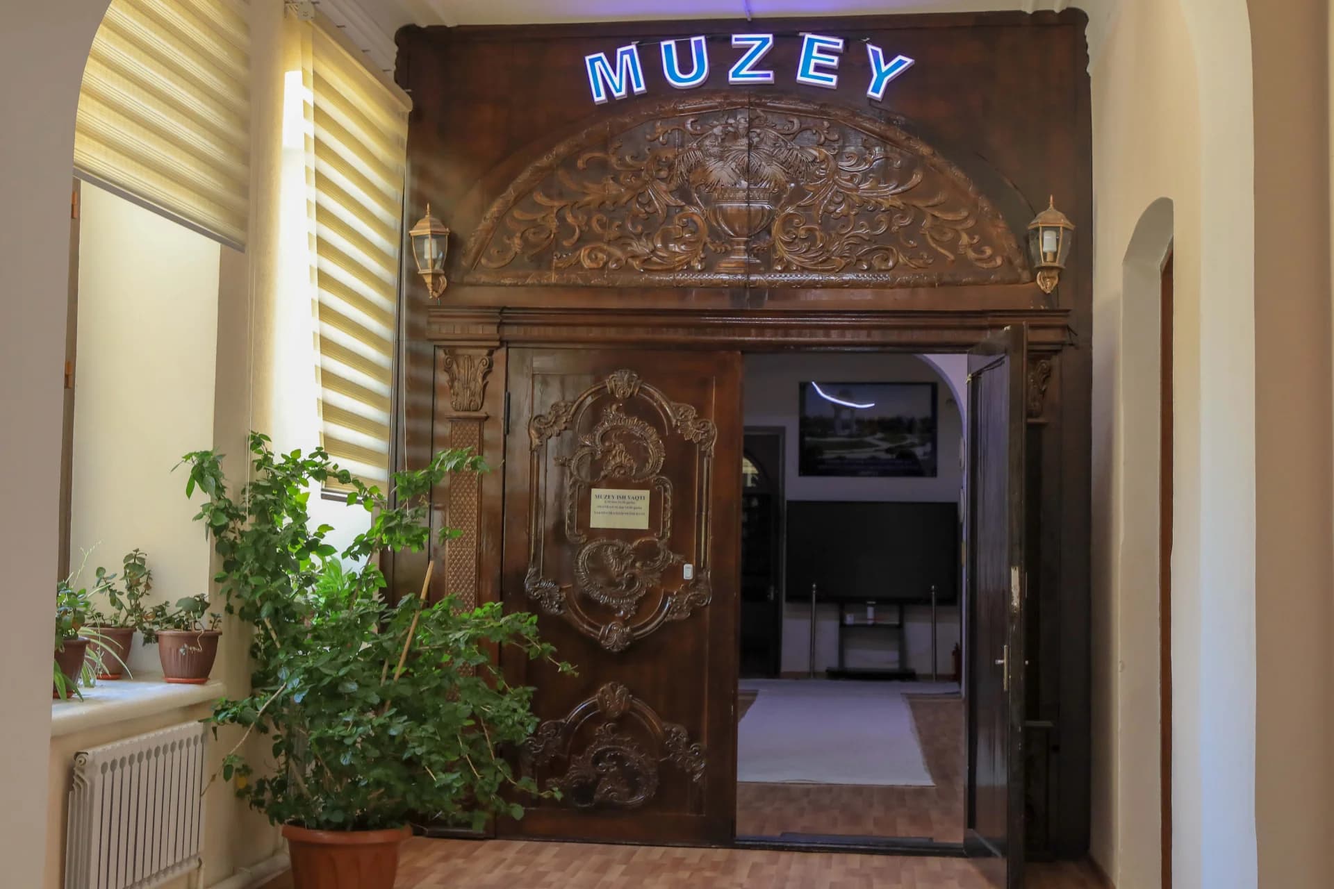 Carved wooden entrance doors with the illuminated sign MUZEY
