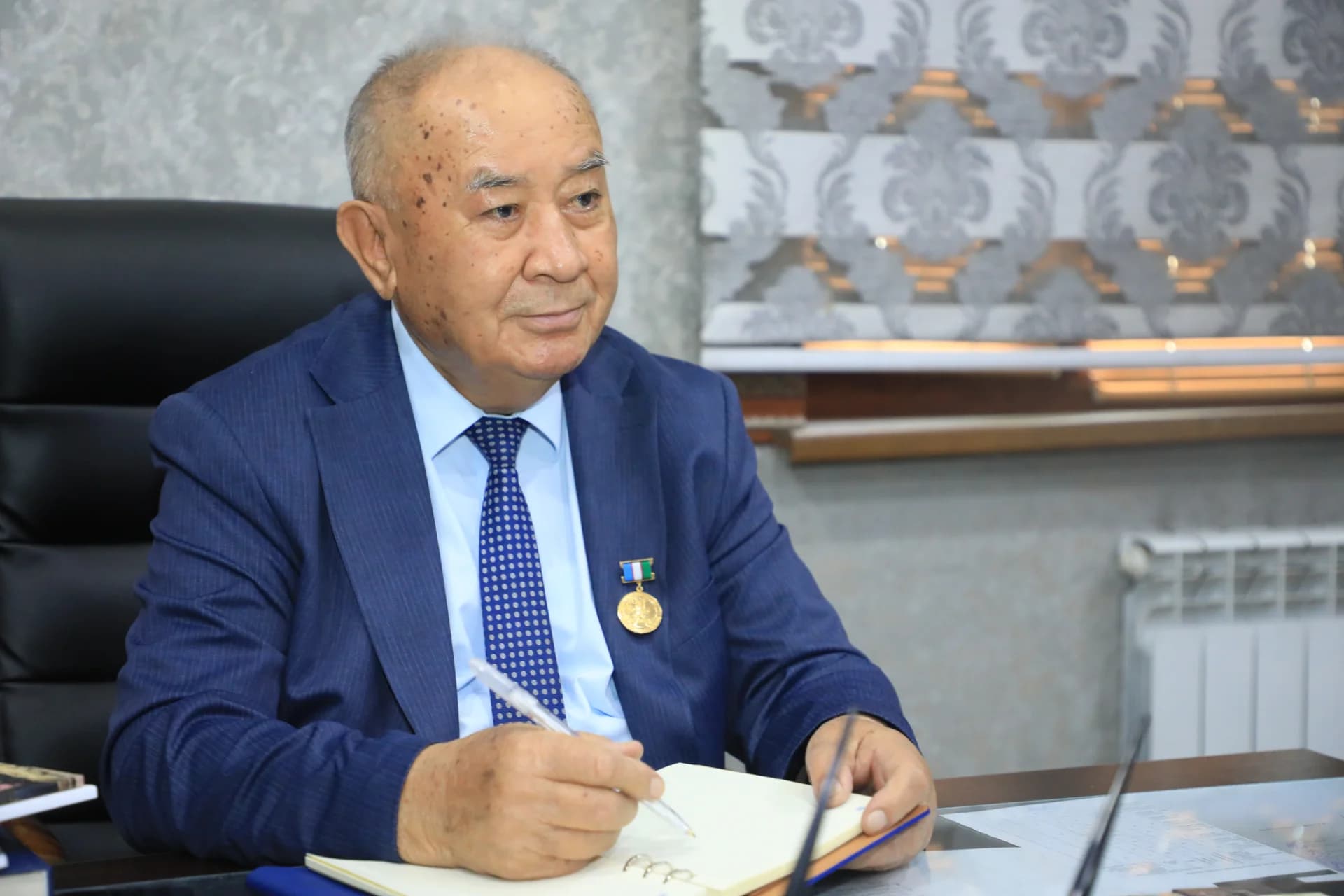 Older man sitting at a desk and writing in a notebook