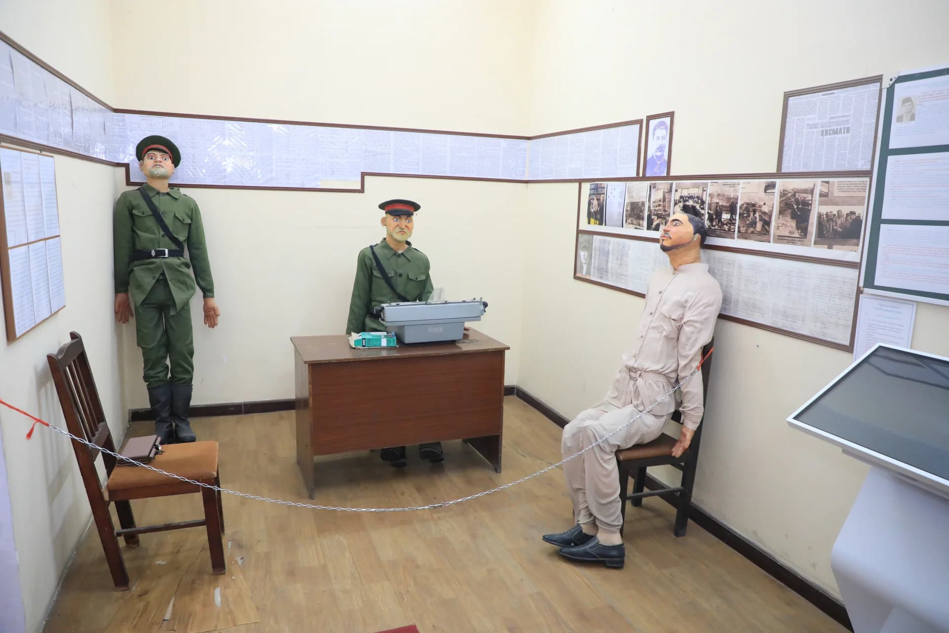 Museum display featuring mannequins in historical uniforms and a chained figure in an interior setting