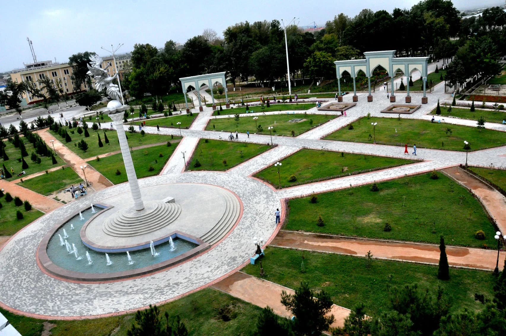 Вид с высокого угла на благоустроенный городской парк с асфальтированными тротуарами, газонами, фонтанами и высоким памятником