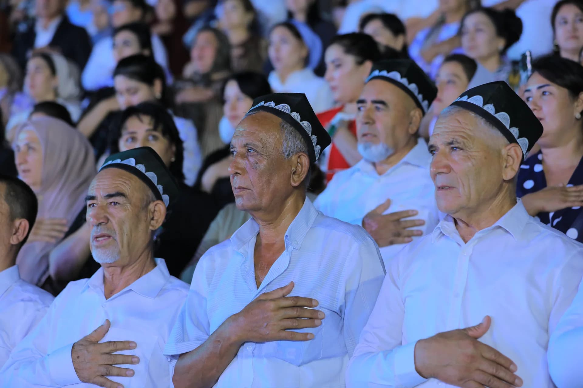 People gathered in an audience with hands placed on chests