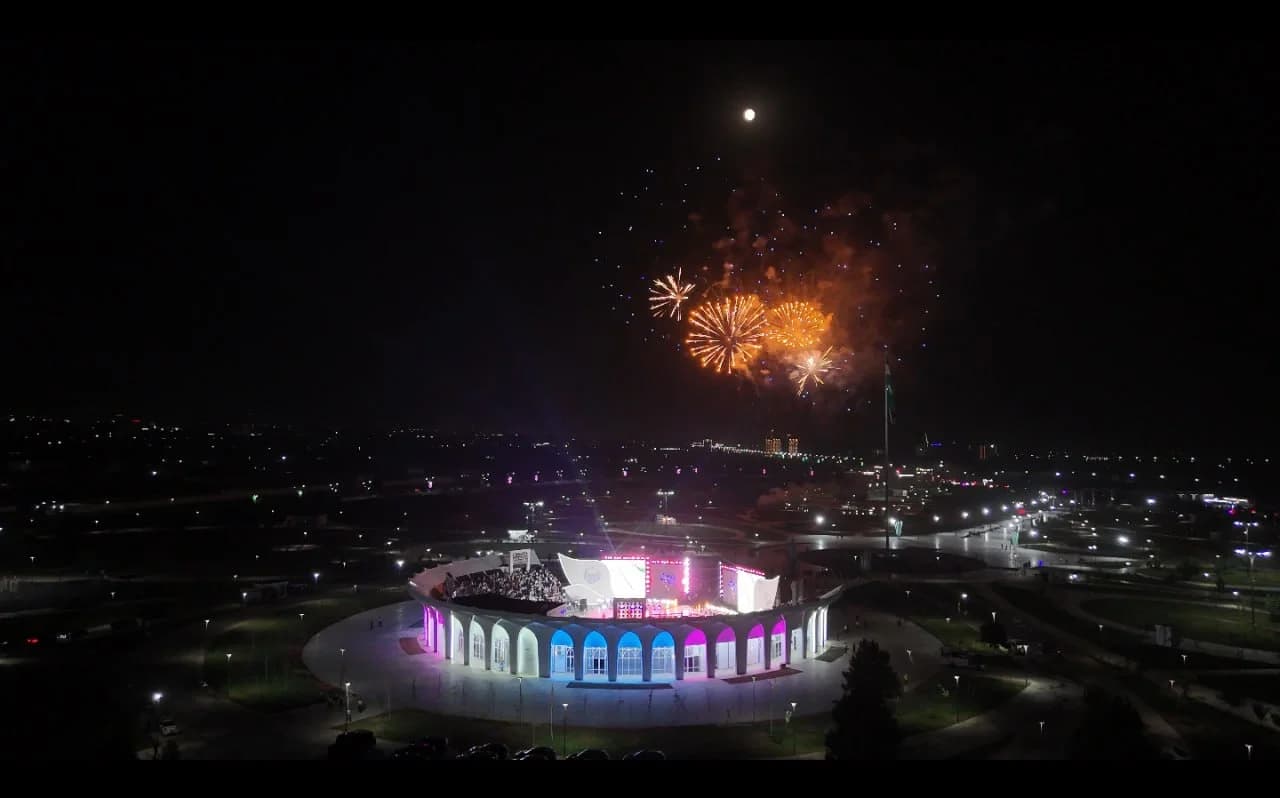Fireworks illuminate night sky over illuminated public structure and surrounding area